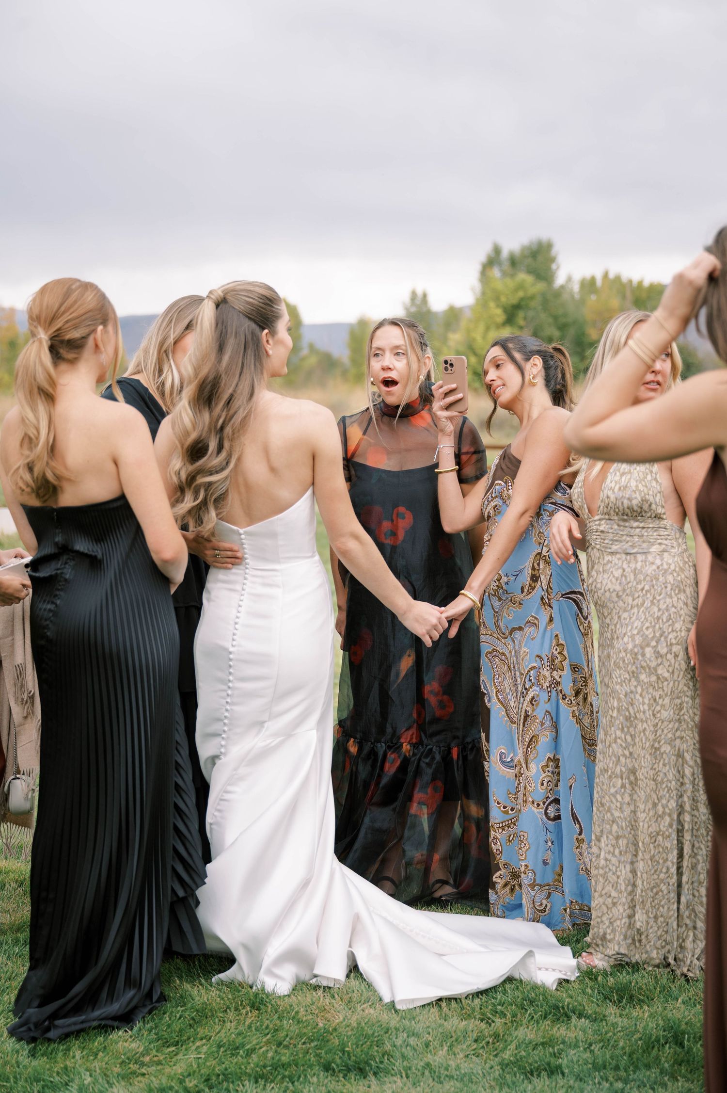 A joyful group in formal attire sharing a candid moment at an outdoor wedding celebration.