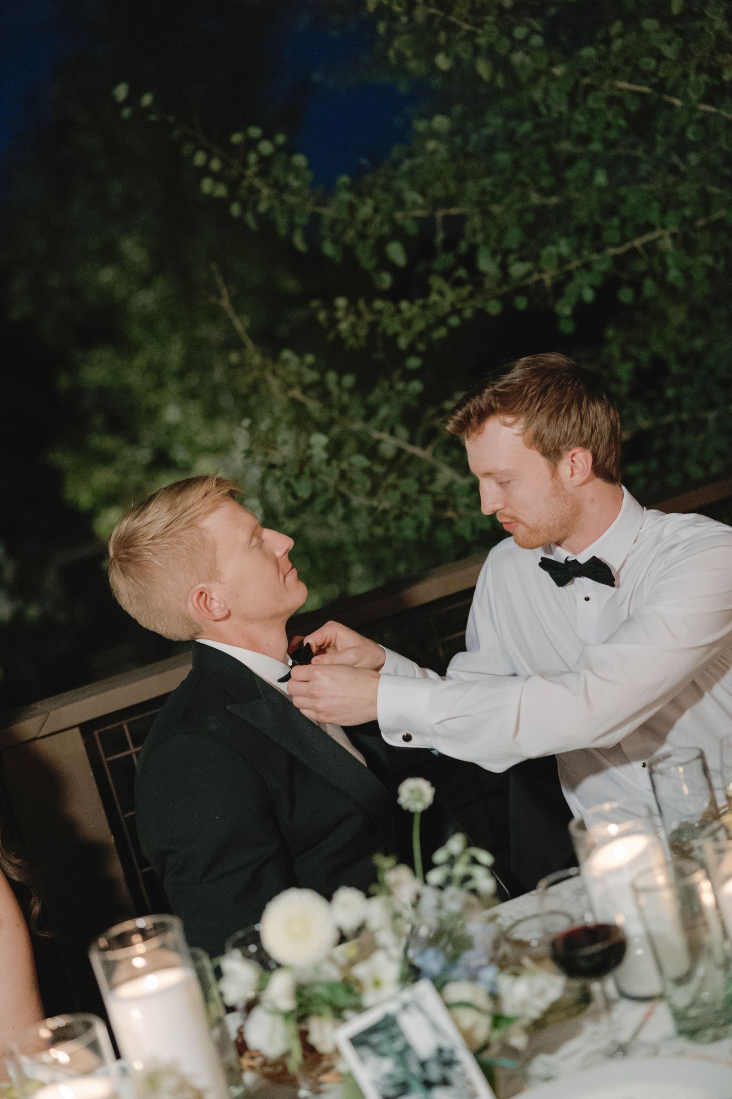 Wedding guests in formal attire sharing playful moments at an outdoor evening reception.