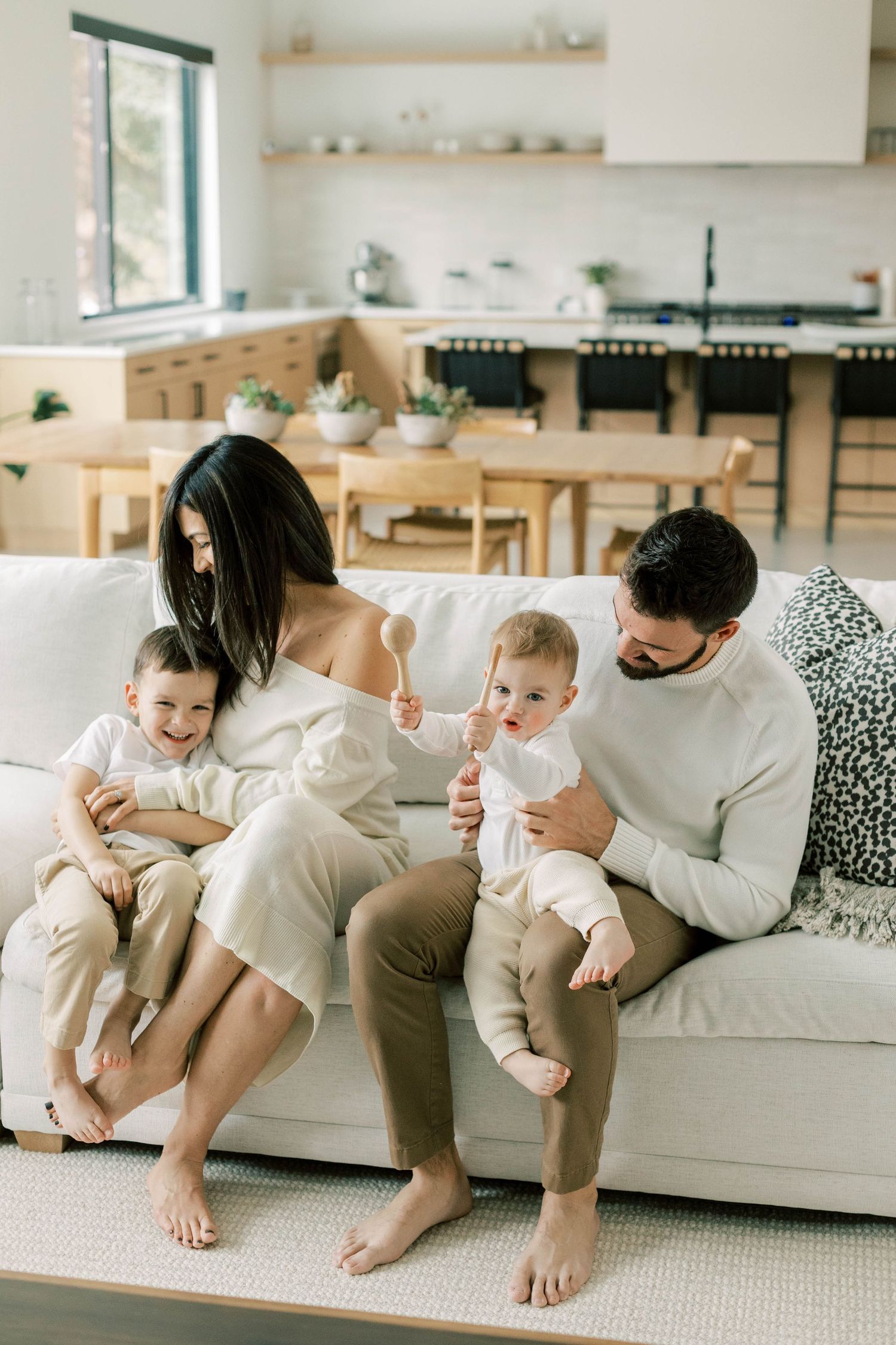 Parents and young children relaxing together on white sofa in bright modern living space.