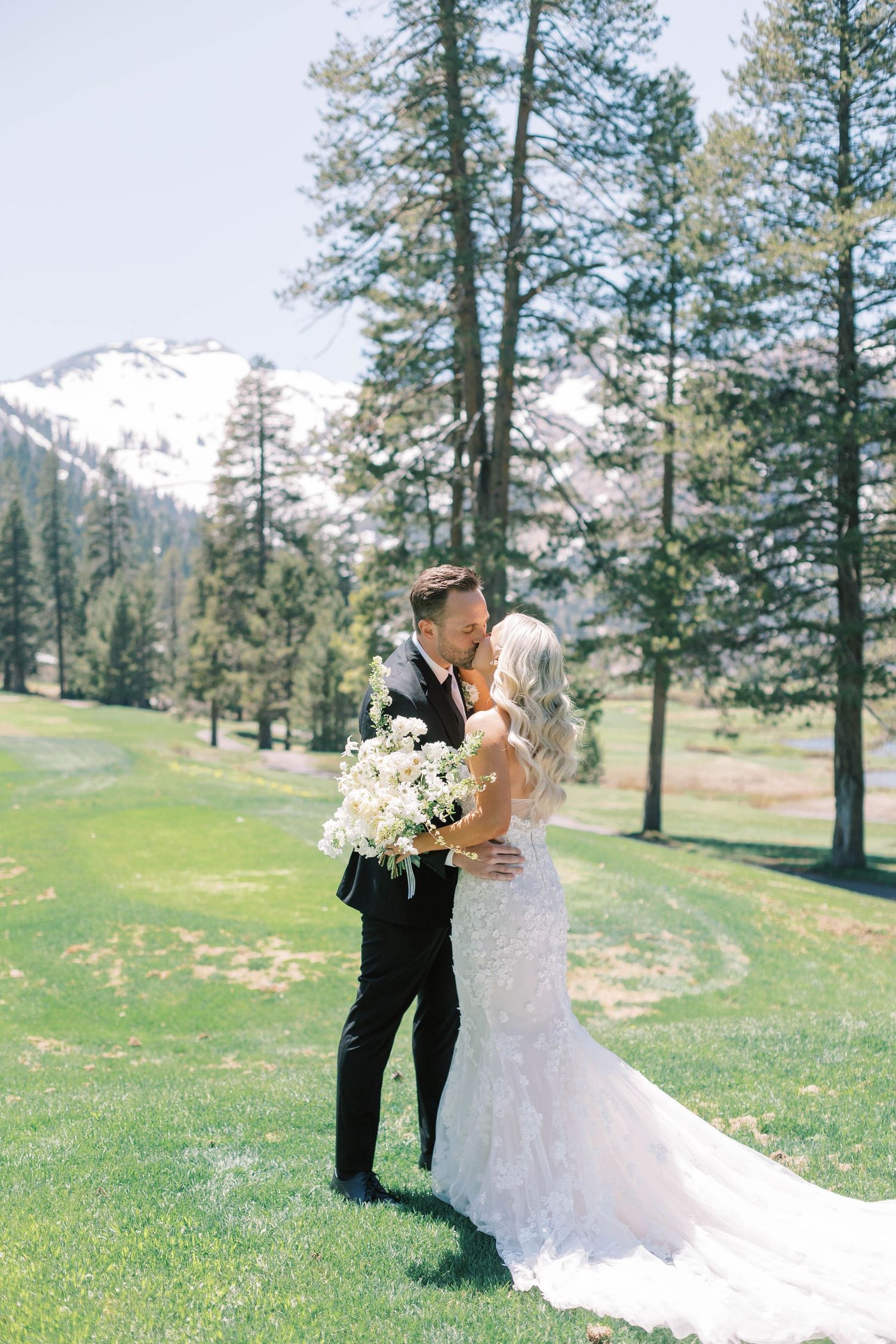 Newlyweds share an intimate moment against a mountain landscape with pine trees.