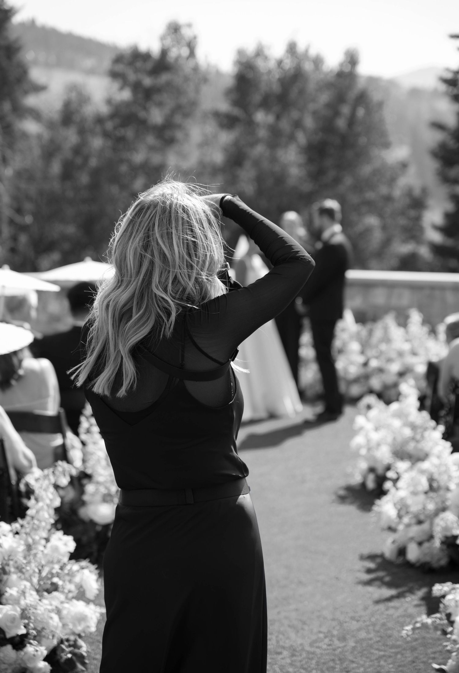 A series of black and white photos showing a person in a black dress dancing joyfully outdoors with white flowers in view.