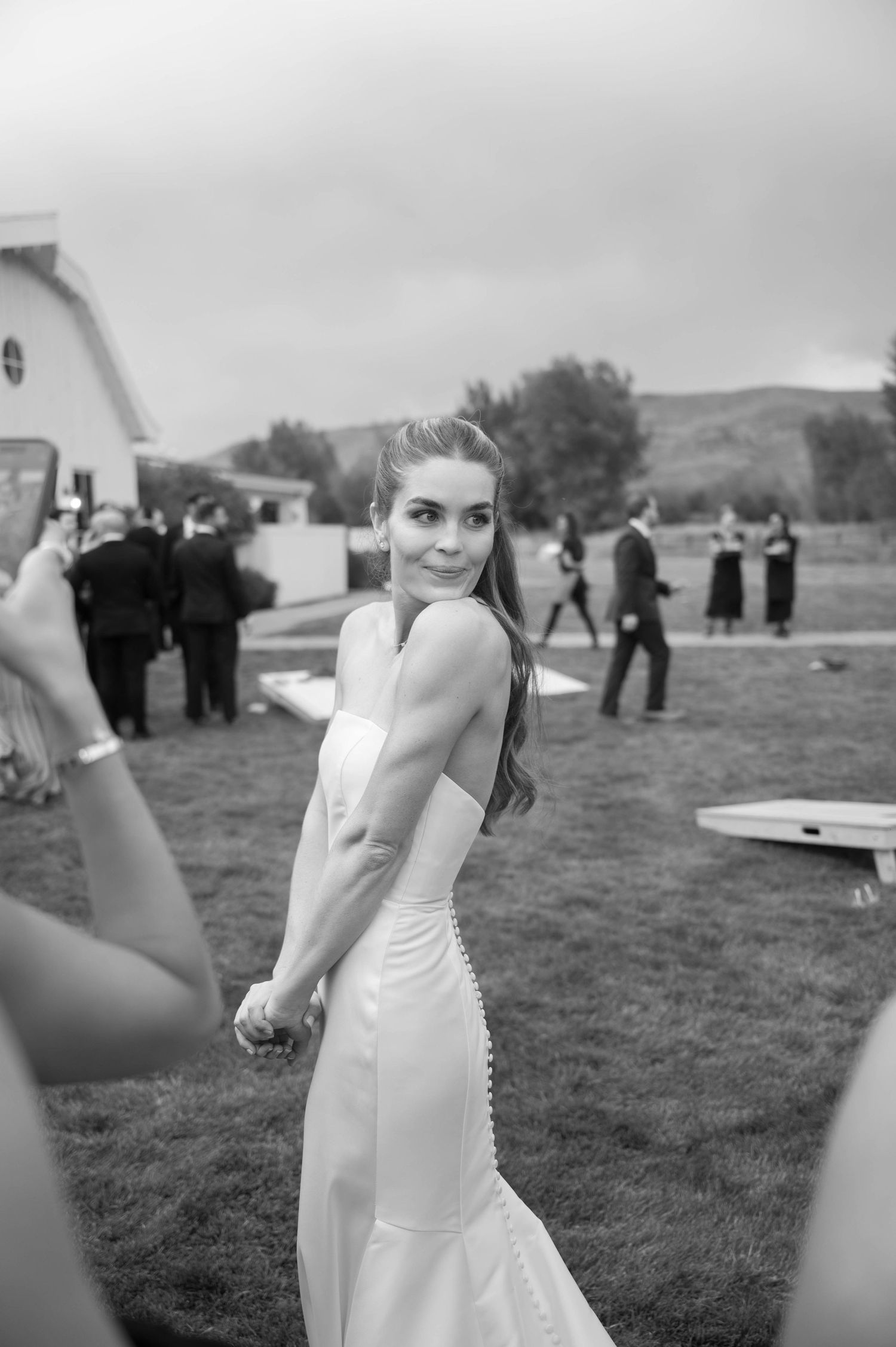 A black and white portrait of a bride in an elegant white dress at an outdoor wedding venue.