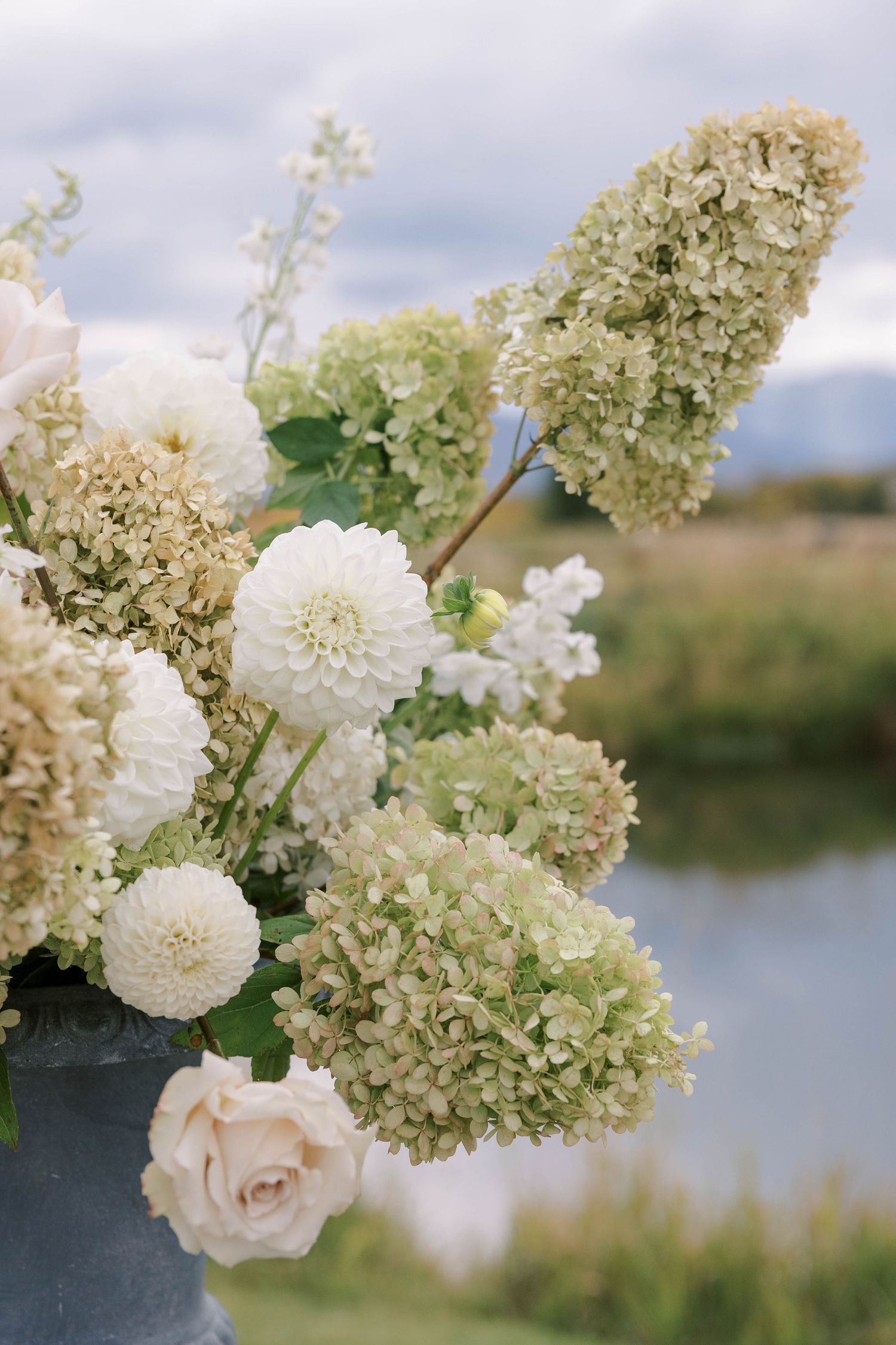 Romantic floral arrangement with white hydrangeas and roses against waterfront backdrop.