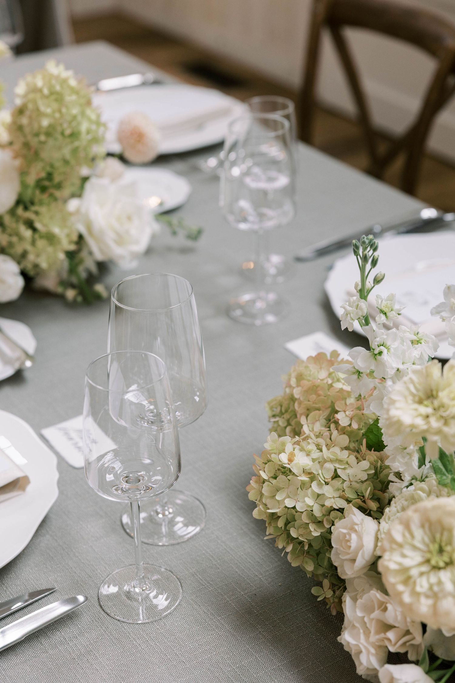 Elegant table setting with white hydrangeas and wine glasses on a light gray linen tablecloth.