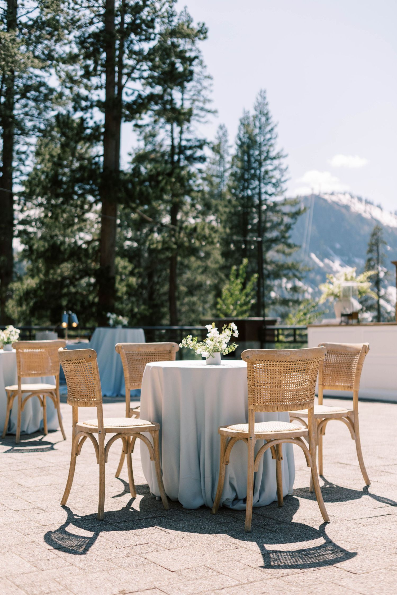 Elegant outdoor dining setup with cane chairs and white tablecloth against mountain scenery at everline resort in lake tahoe.