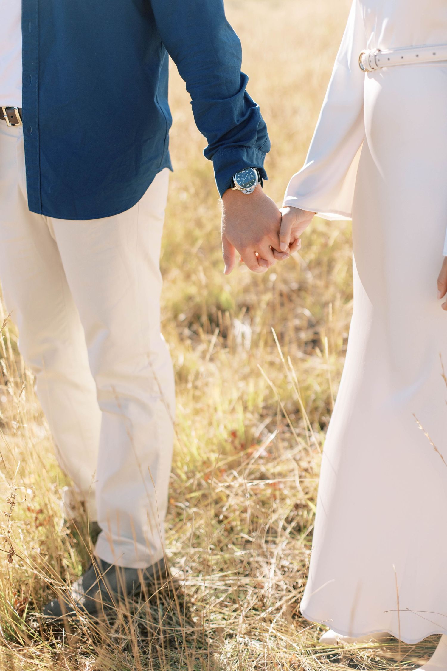 Close-up of couple holding hands while walking through golden grass field.