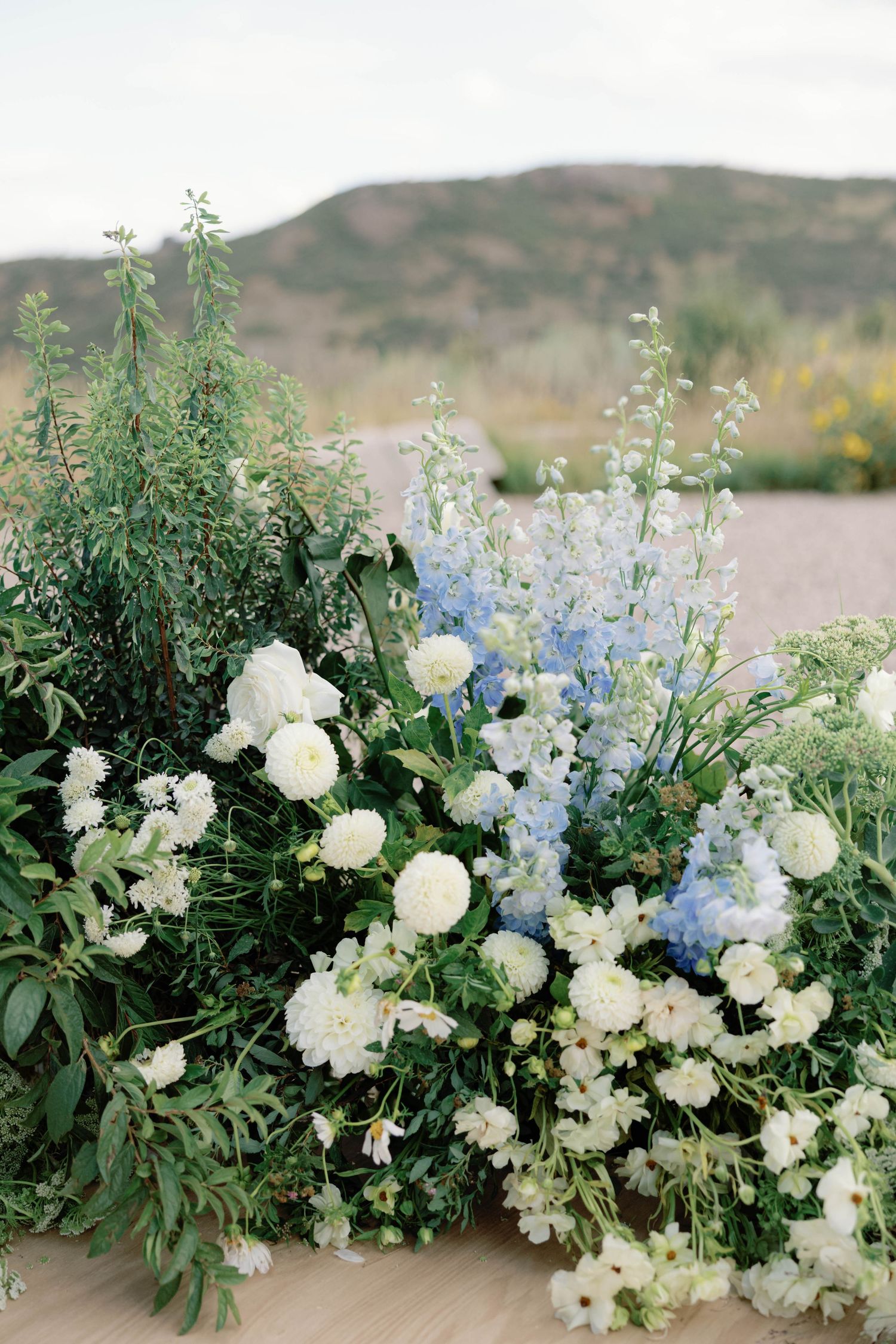 Elegant floral arrangement featuring white and blue blooms with greenery against a mountain backdrop.