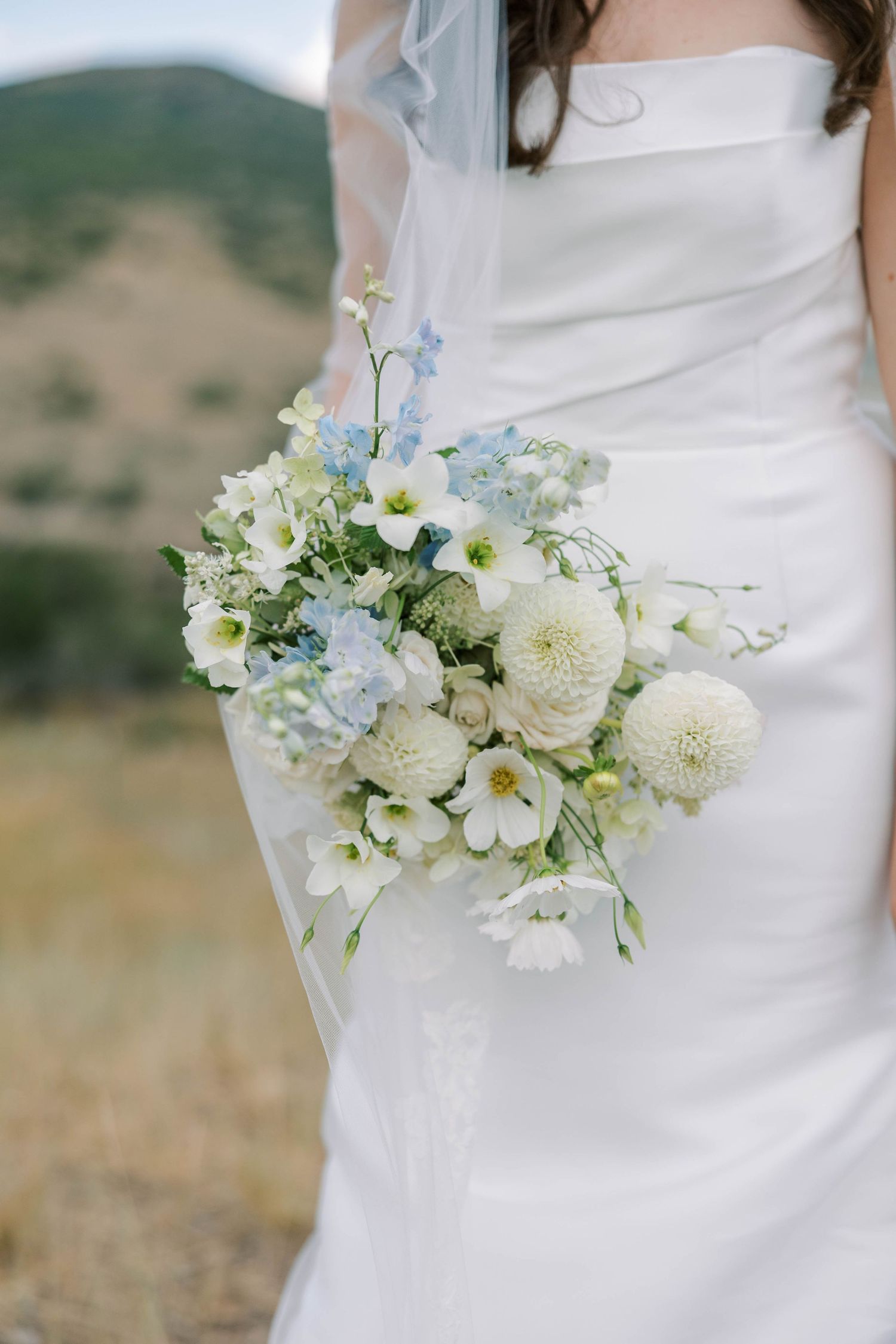 Close-up details of white and blue floral wedding bouquet with roses and delicate blooms.