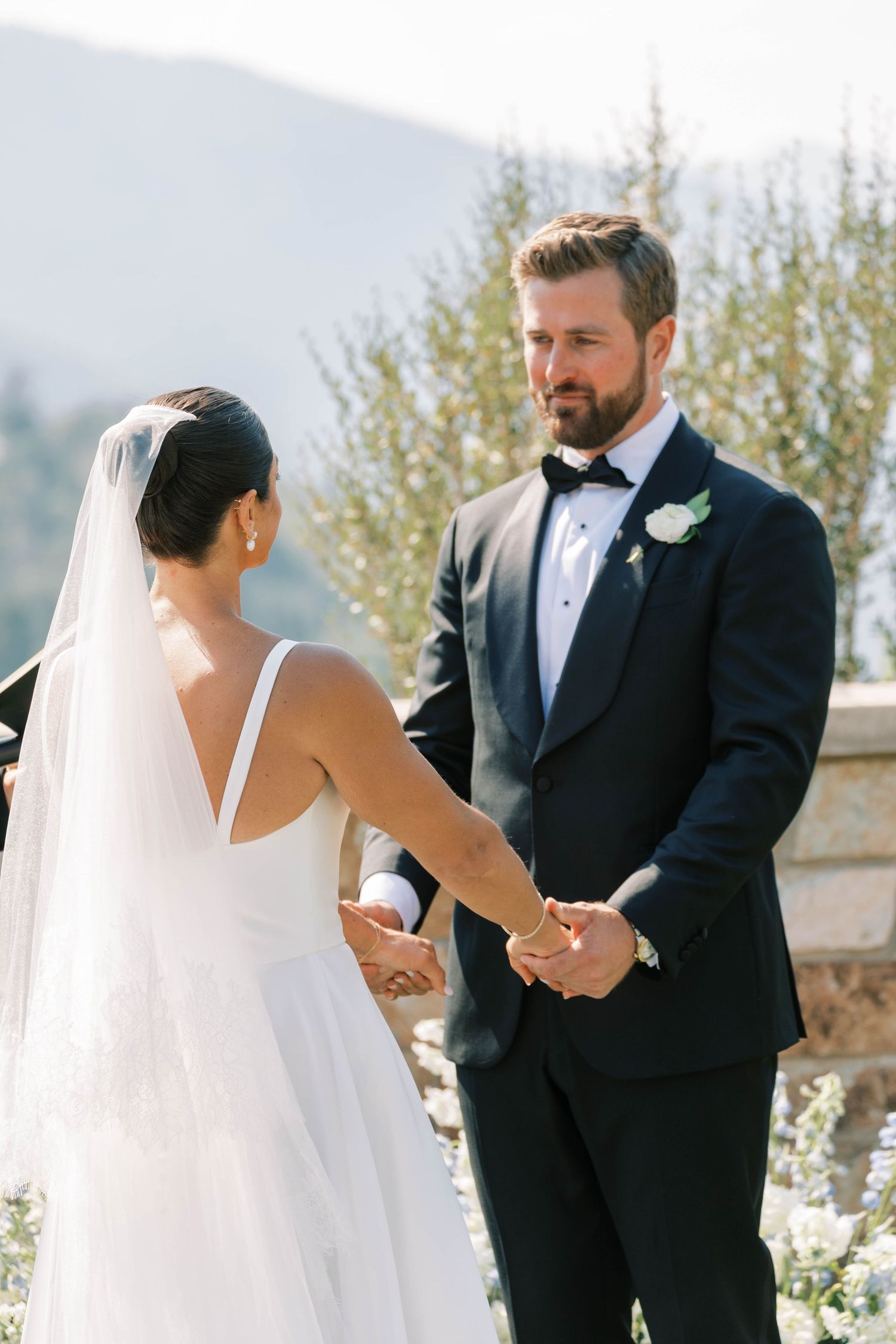 A bride and groom share a tender moment during their outdoor wedding ceremony on a sunny day.