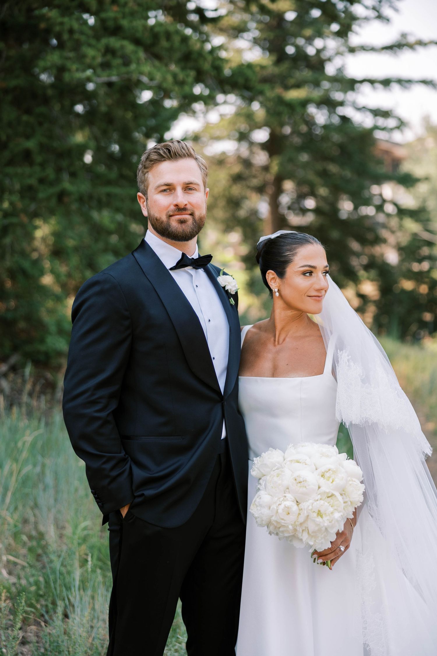 Elegant bride and groom pose together in outdoor wedding portraits with natural greenery backdrop.