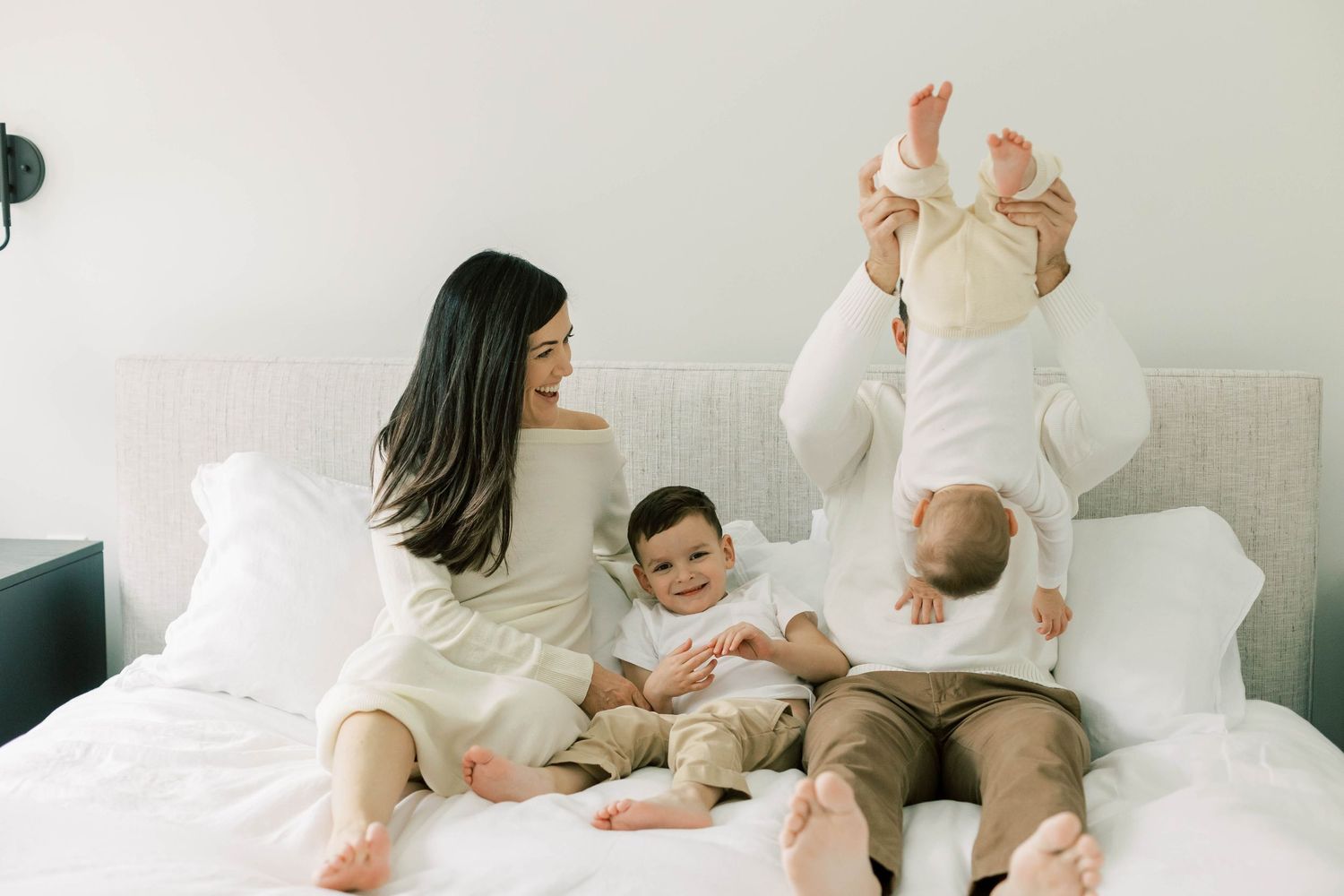 Family sharing playful moment together on white bed.