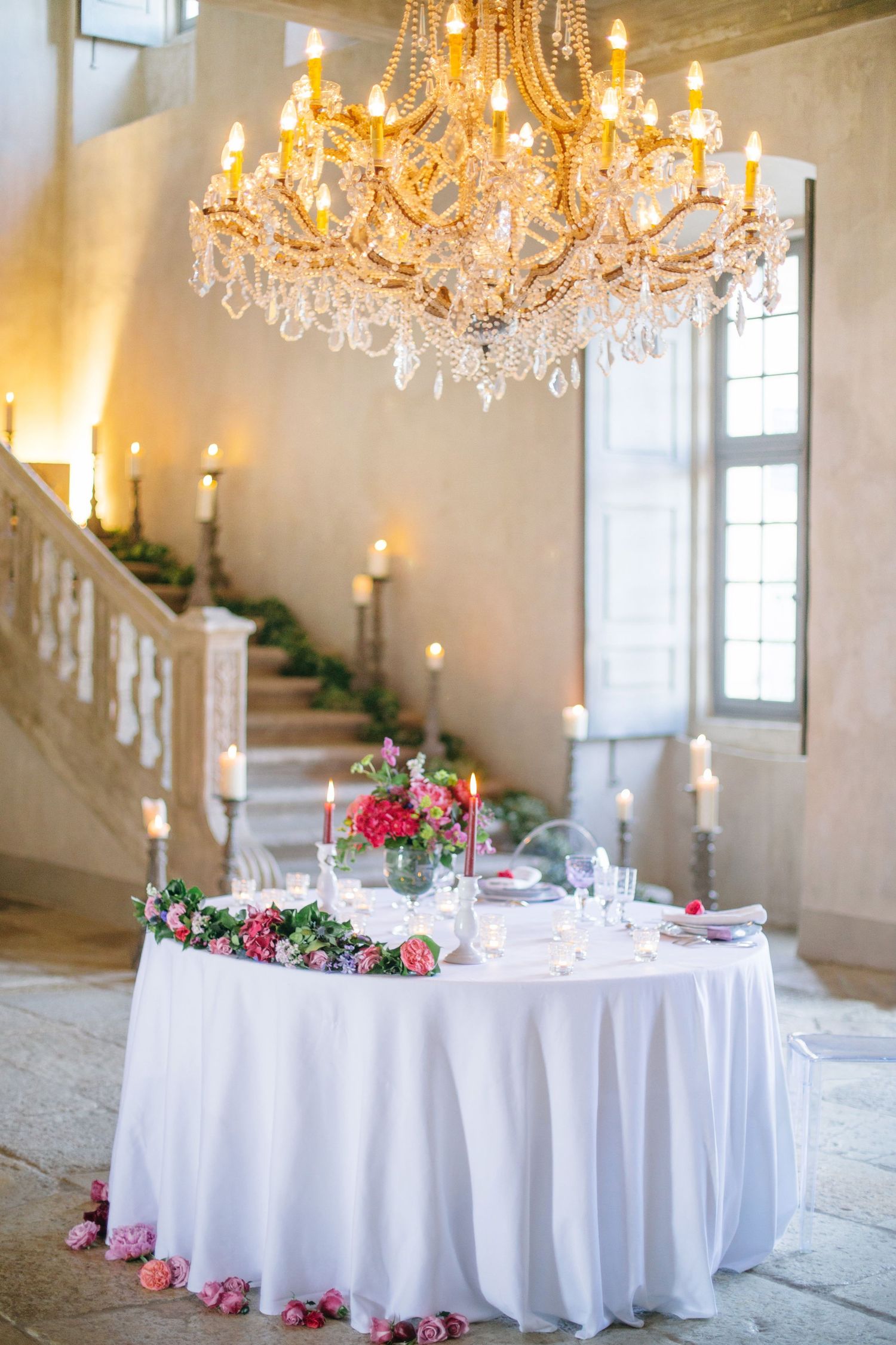 Elegant wedding reception table with white linens, floral arrangements and crystal chandelier in a grand venue at chateau de moissac.