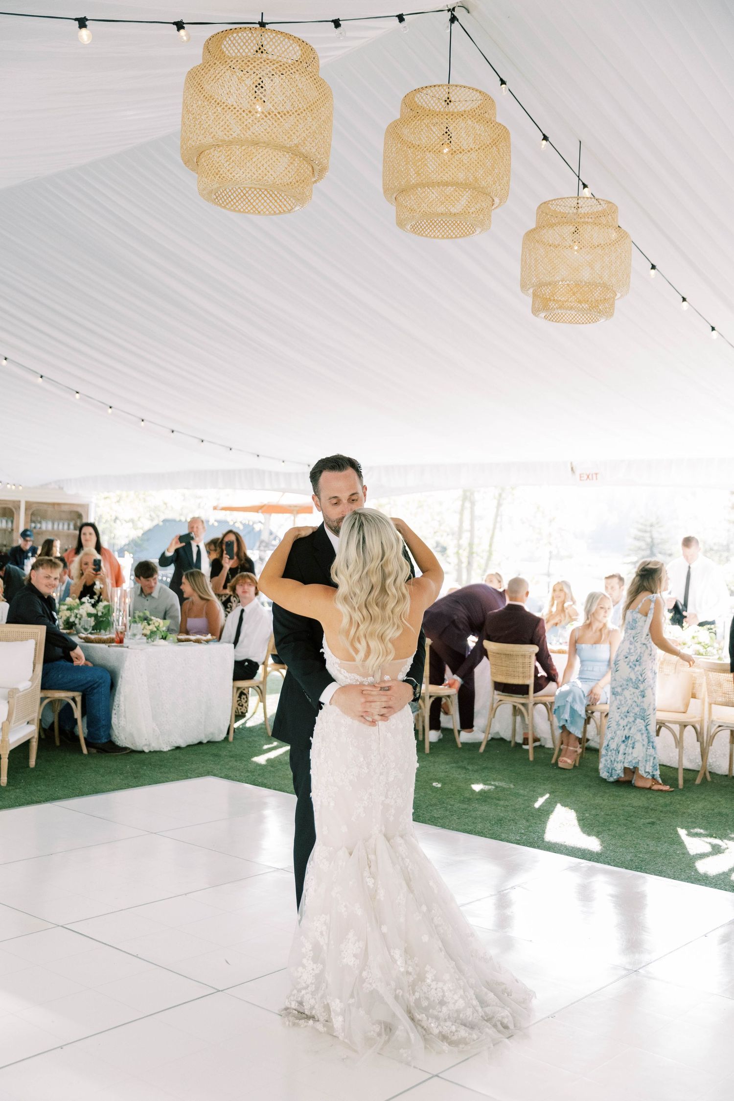 First dance moment under woven rattan pendant lights at an outdoor tented wedding reception.