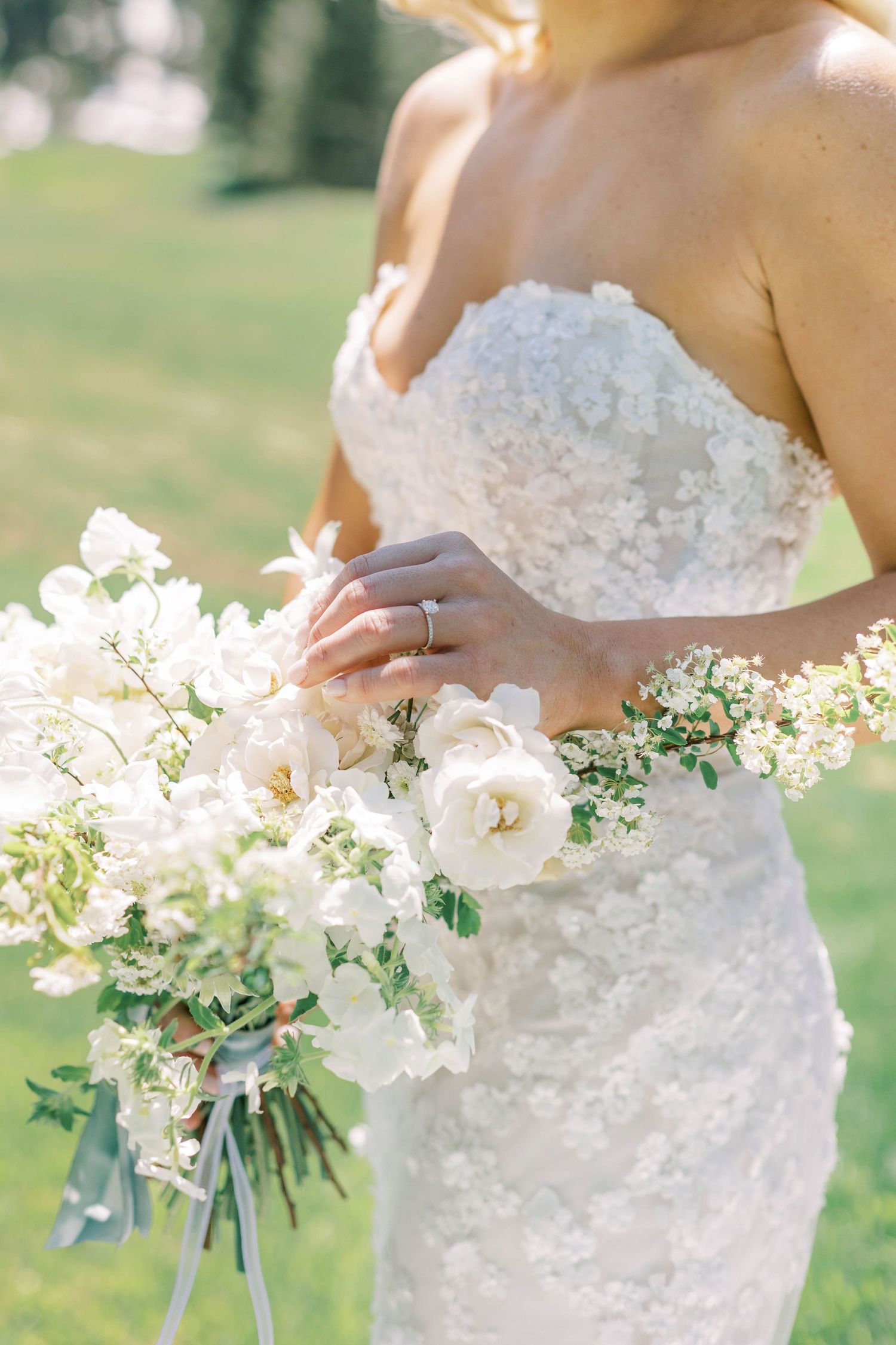 Detail shot of a lace wedding dress and white rose bouquet in natural sunlight.
