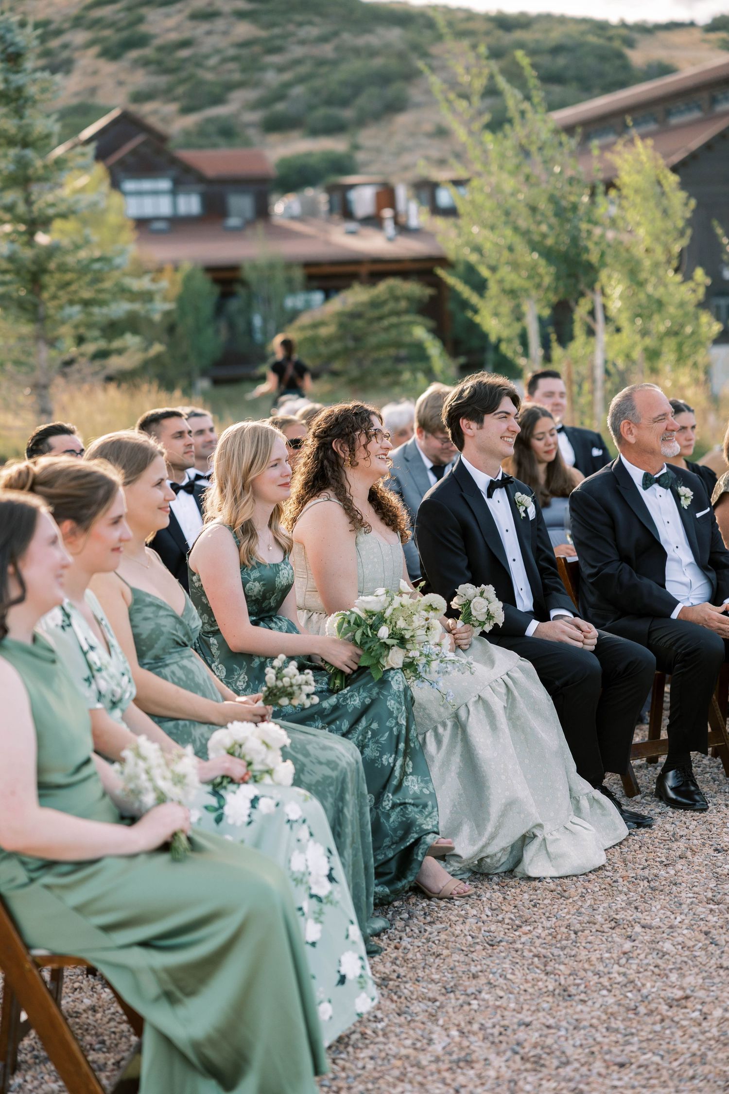 Wedding guests in sage green dresses and formal attire seated in rows at an outdoor ceremony.