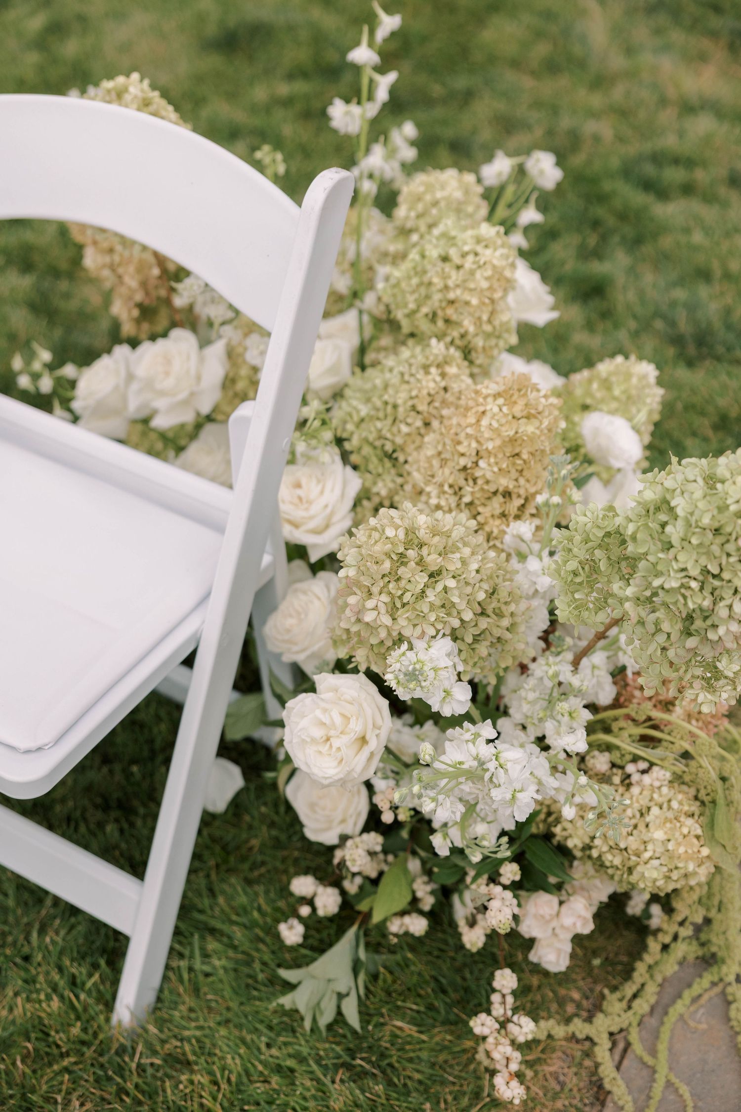 White wedding ceremony chairs decorated with lush hydrangea and rose floral arrangements.
