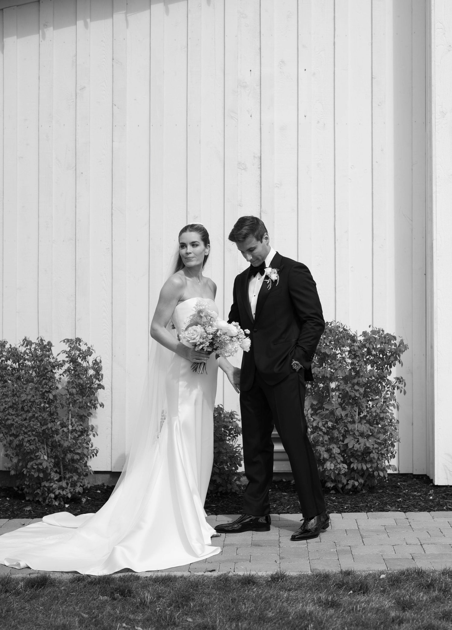 A black and white wedding photo series showing a couple posing against a white wall with greenery in four artistic shots.