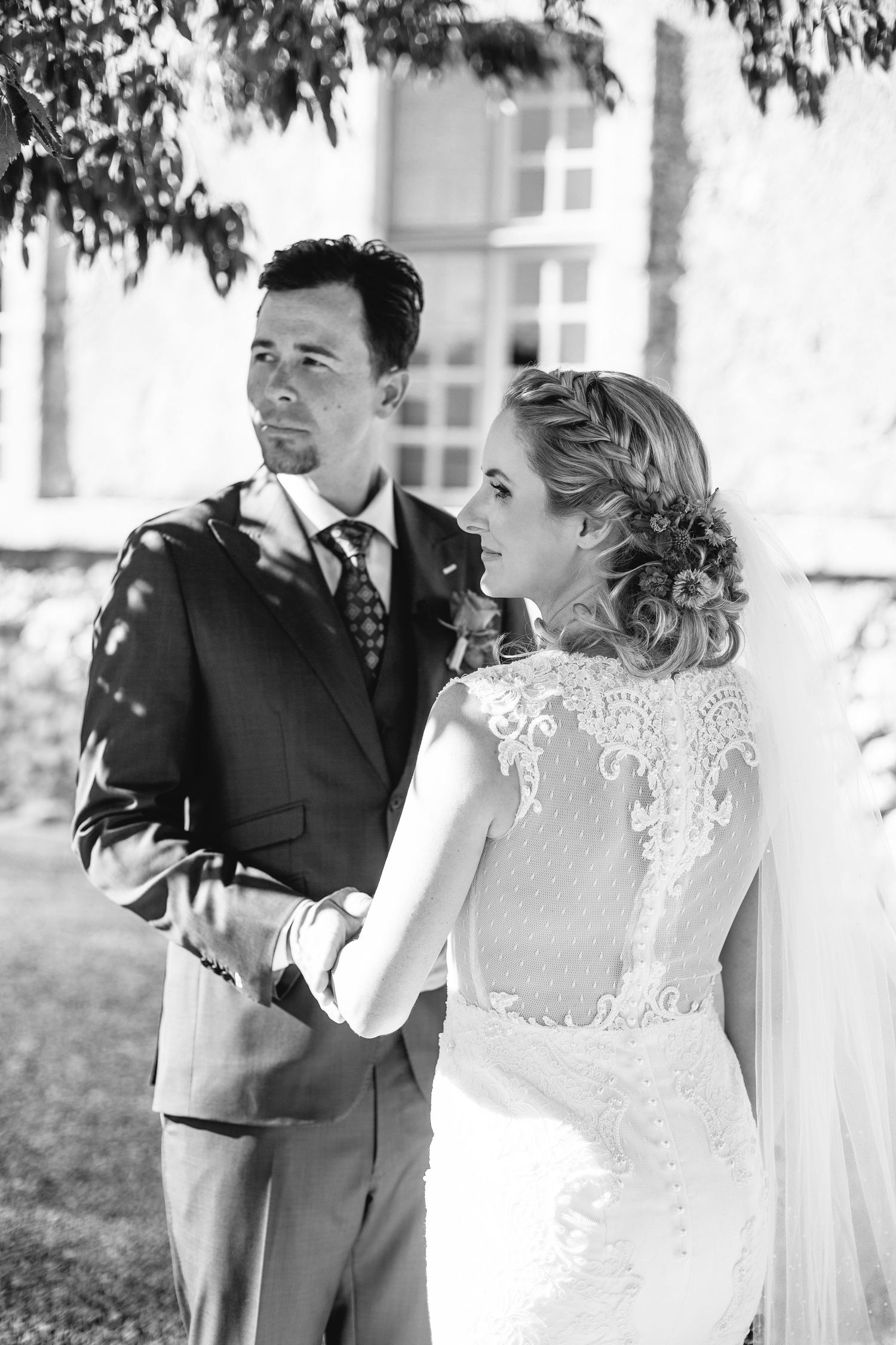 A romantic black and white wedding photo showing a couple in formal attire under dappled sunlight.