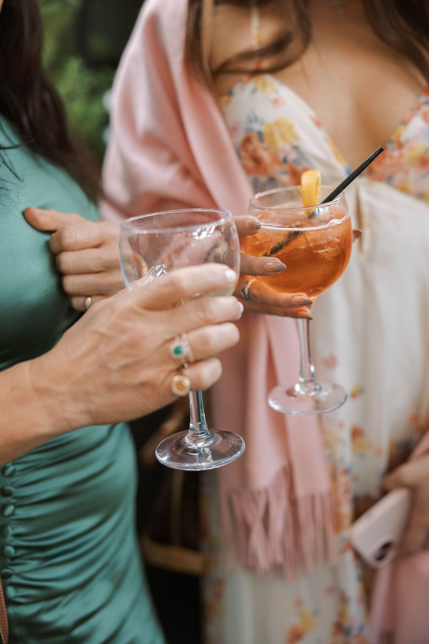 People in pink and green attire hold elegant cocktail glasses at a social gathering.