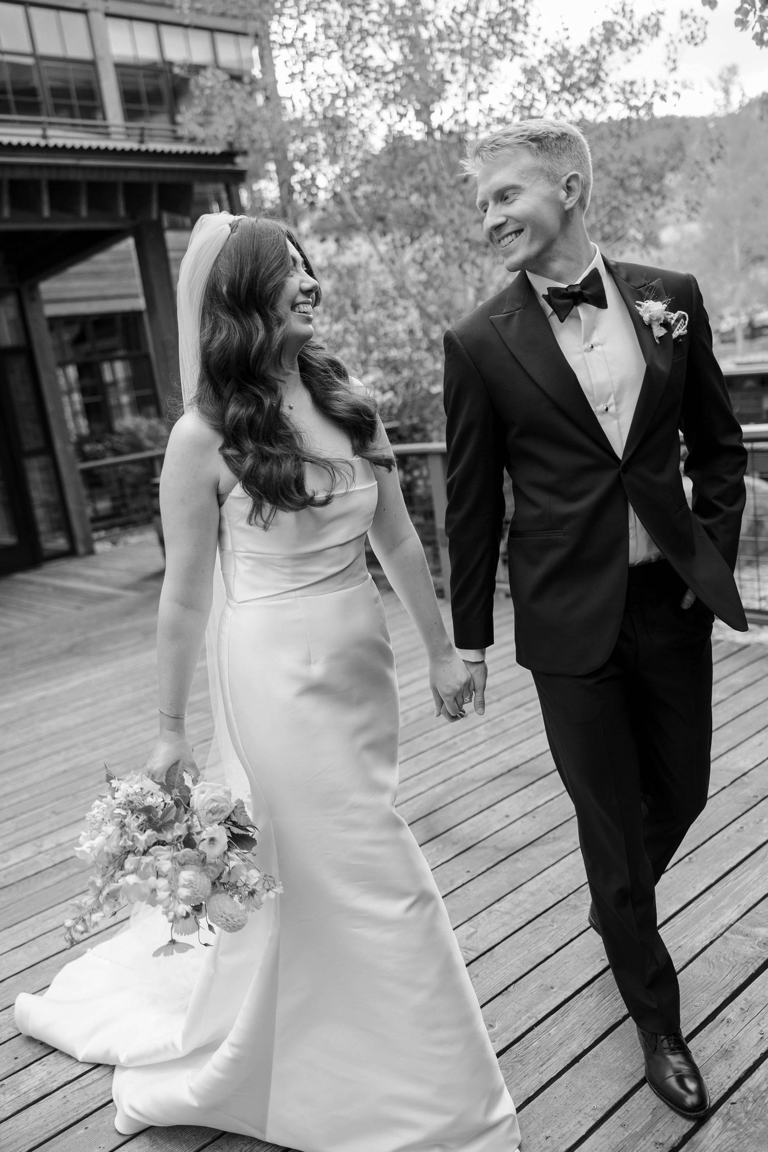 Wedding couple walking together on a wooden boardwalk in formal attire.
