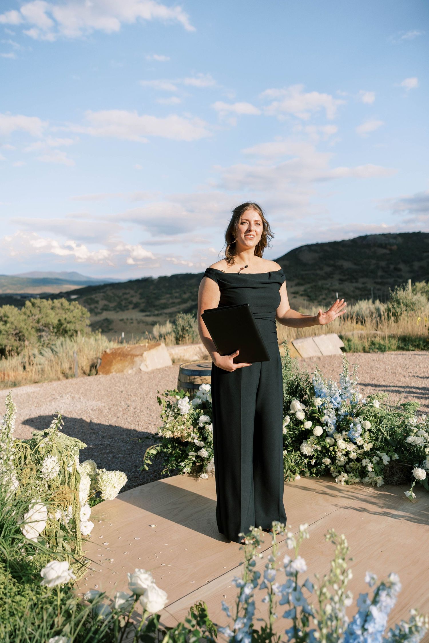 Wedding ceremony setup with wooden platform and floral arrangements against mountain backdrop.