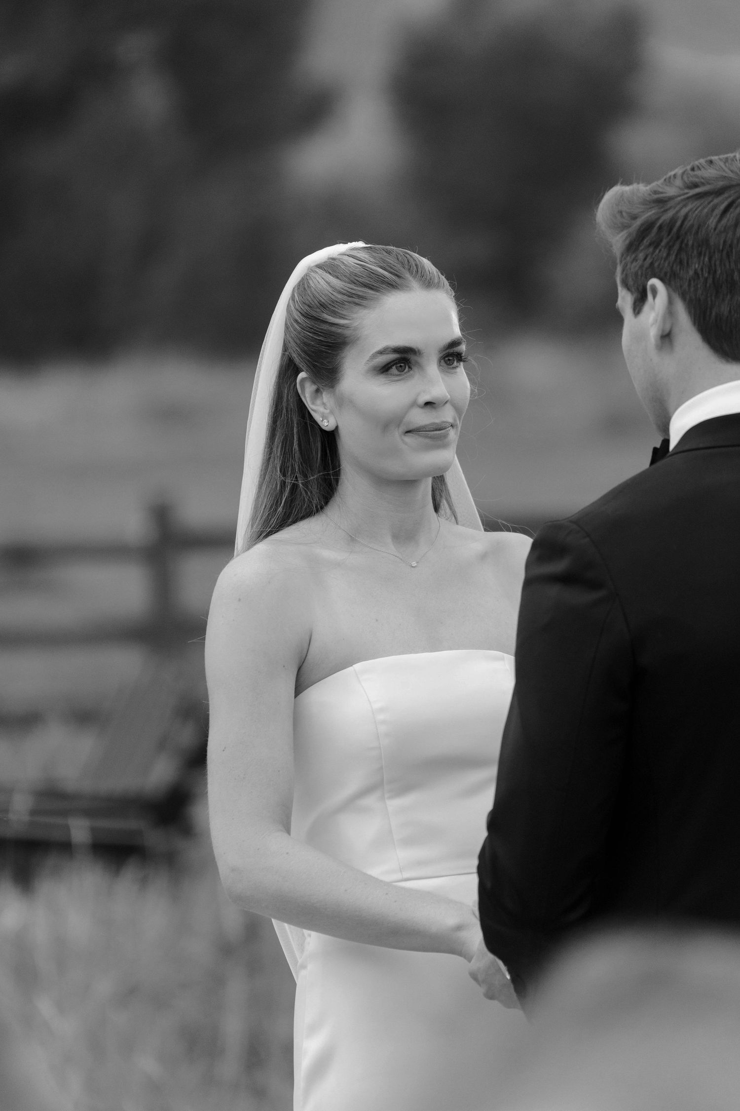 Black and white wedding portrait showing bride and groom in an intimate outdoor setting with soft focus background.
