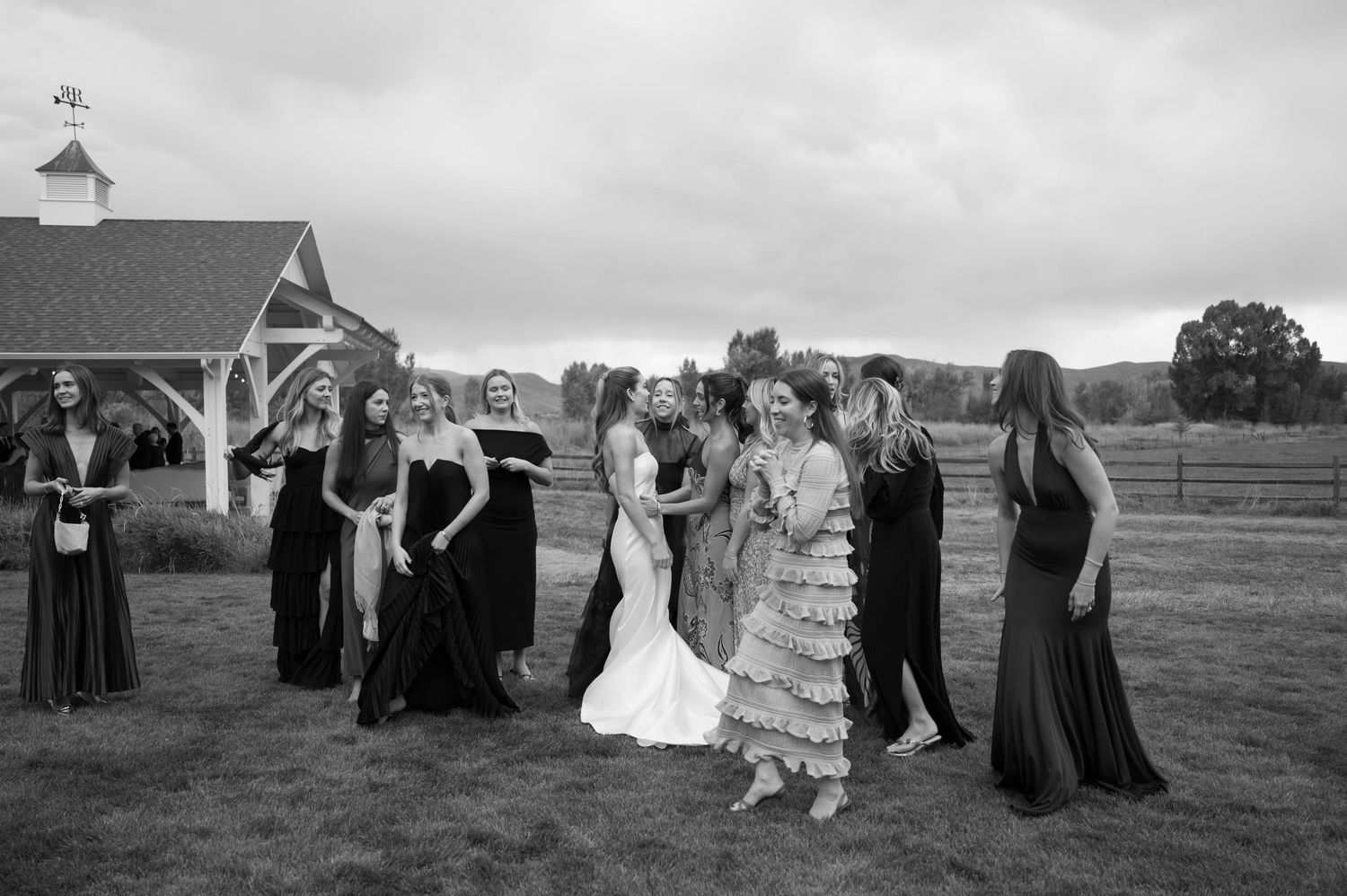 Wedding party guests dance and celebrate outdoors in a scenic field during sunset.
