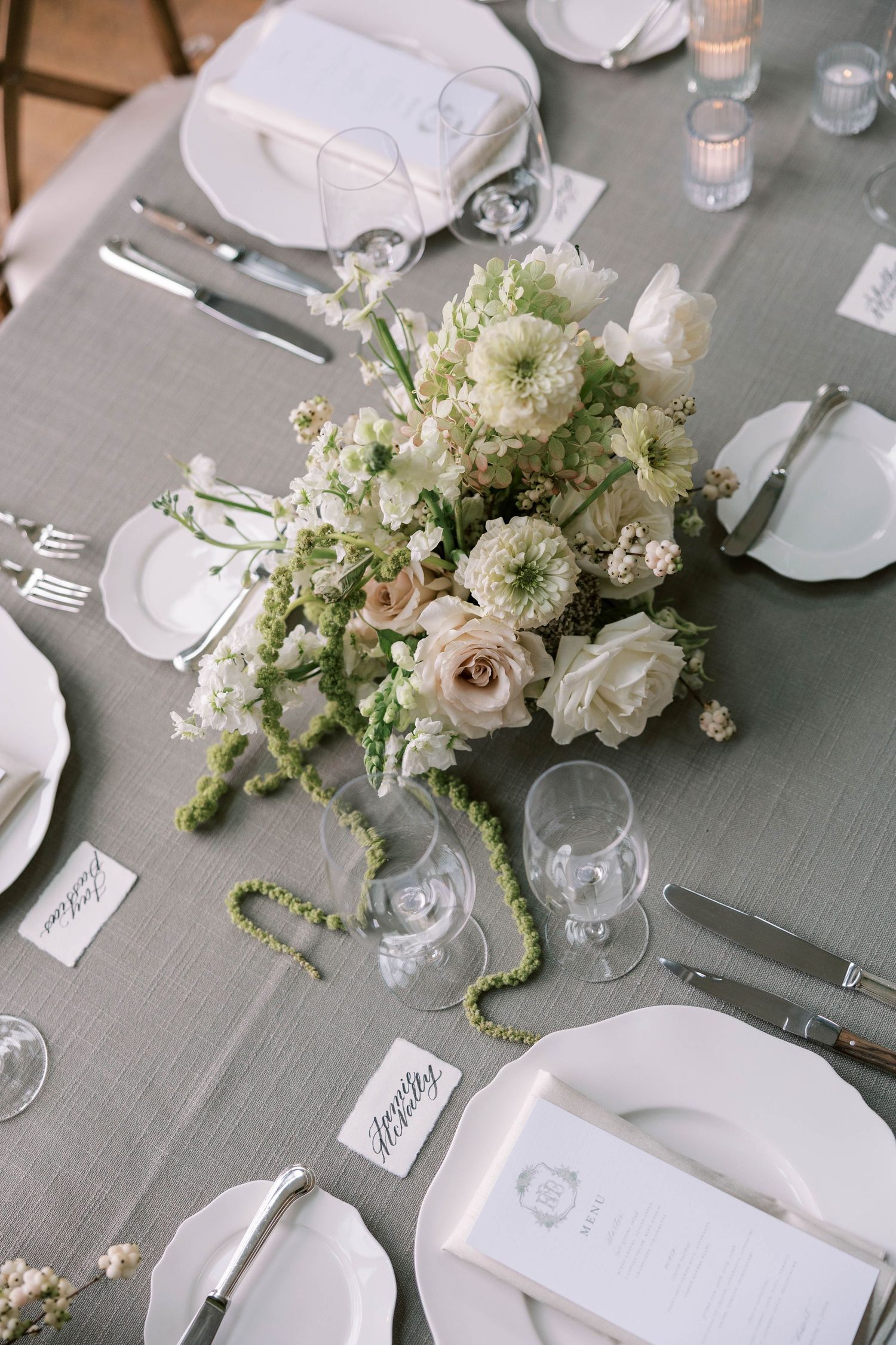 Elegant wedding table setting with white floral centerpieces, grey linens, and crystal glassware arranged in a formal style.