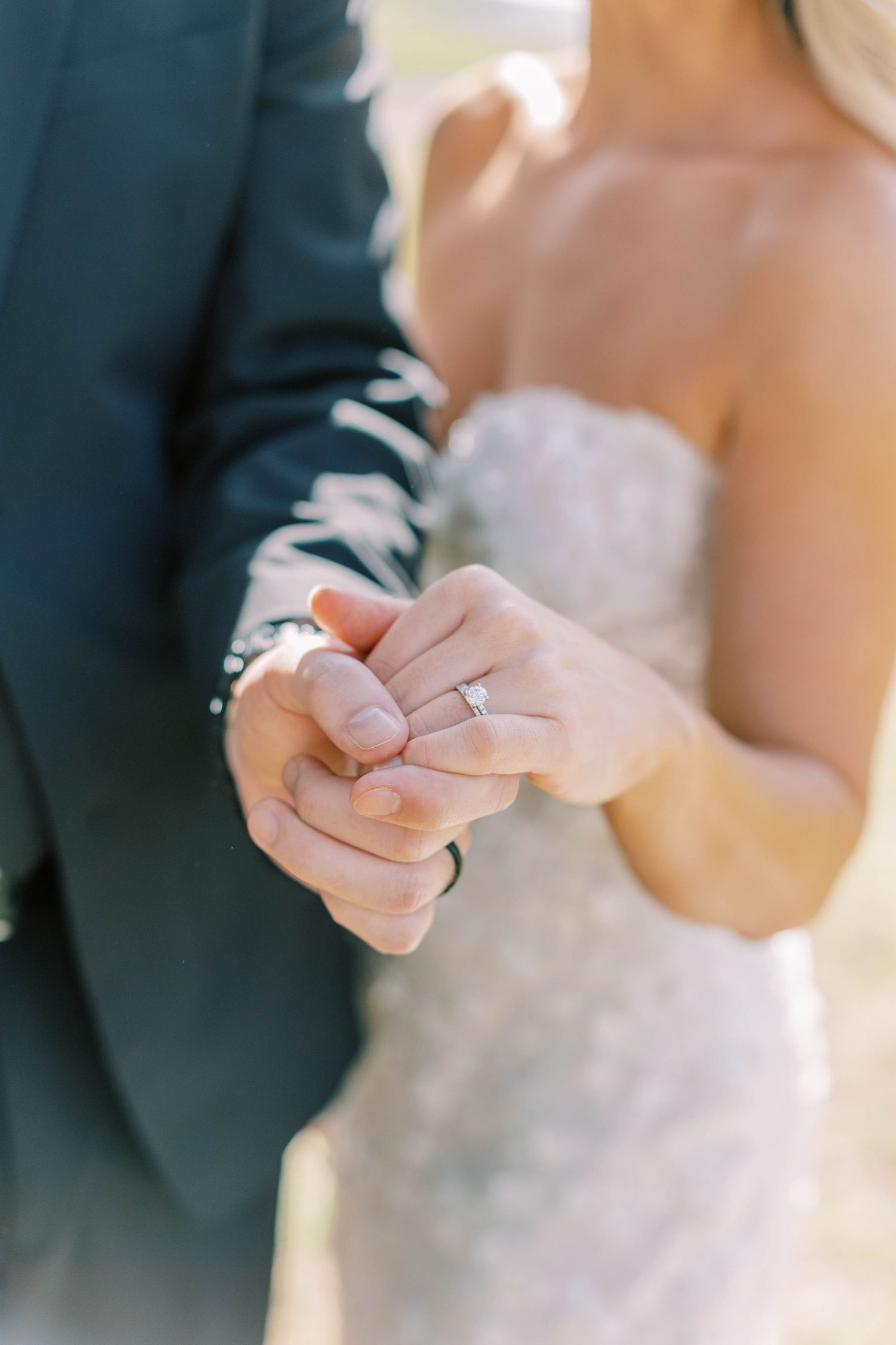 Close-up of couple's clasped hands showing engagement ring during outdoor wedding ceremony.