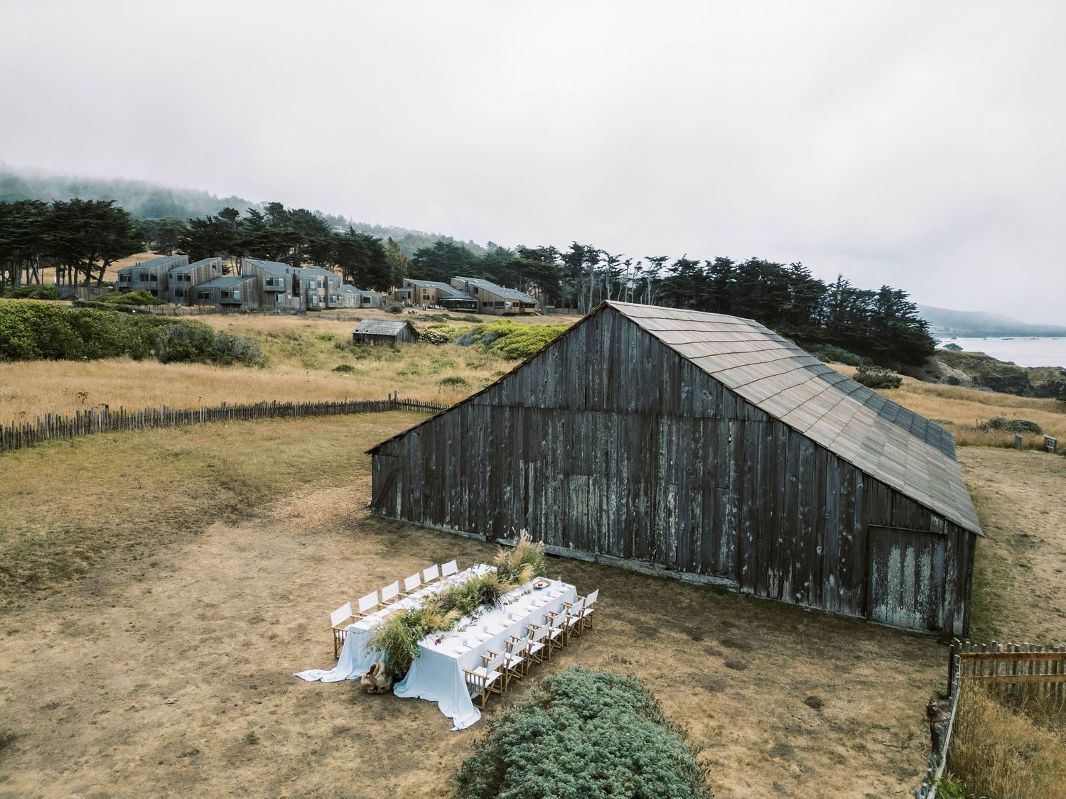 Panoramic sequence of weathered wooden barns and rustic farm buildings along a rural coastal landscape.