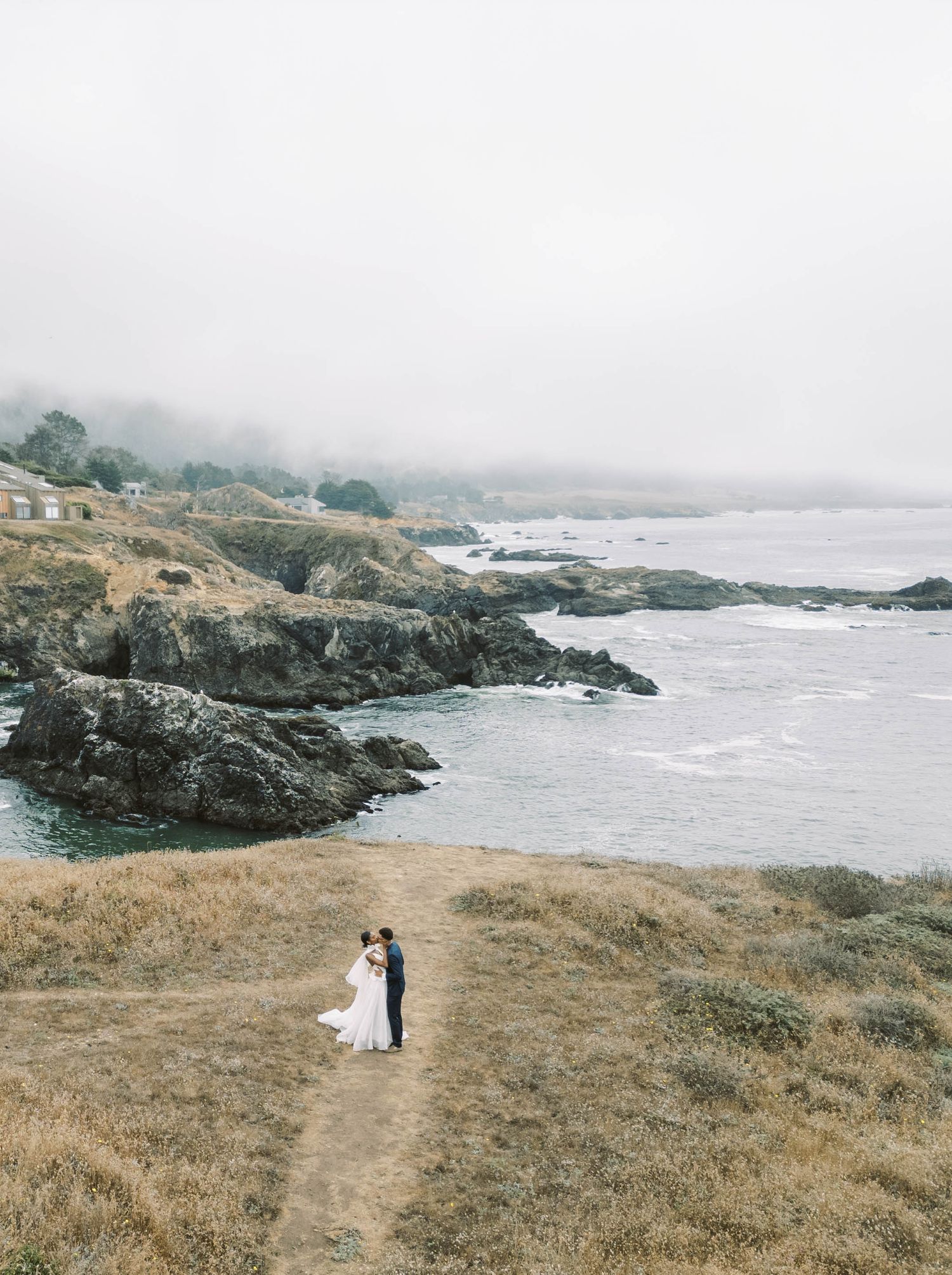 A scenic coastal landscape view of rocky cliffs and misty shoreline at Fort Ross, California on an overcast day.