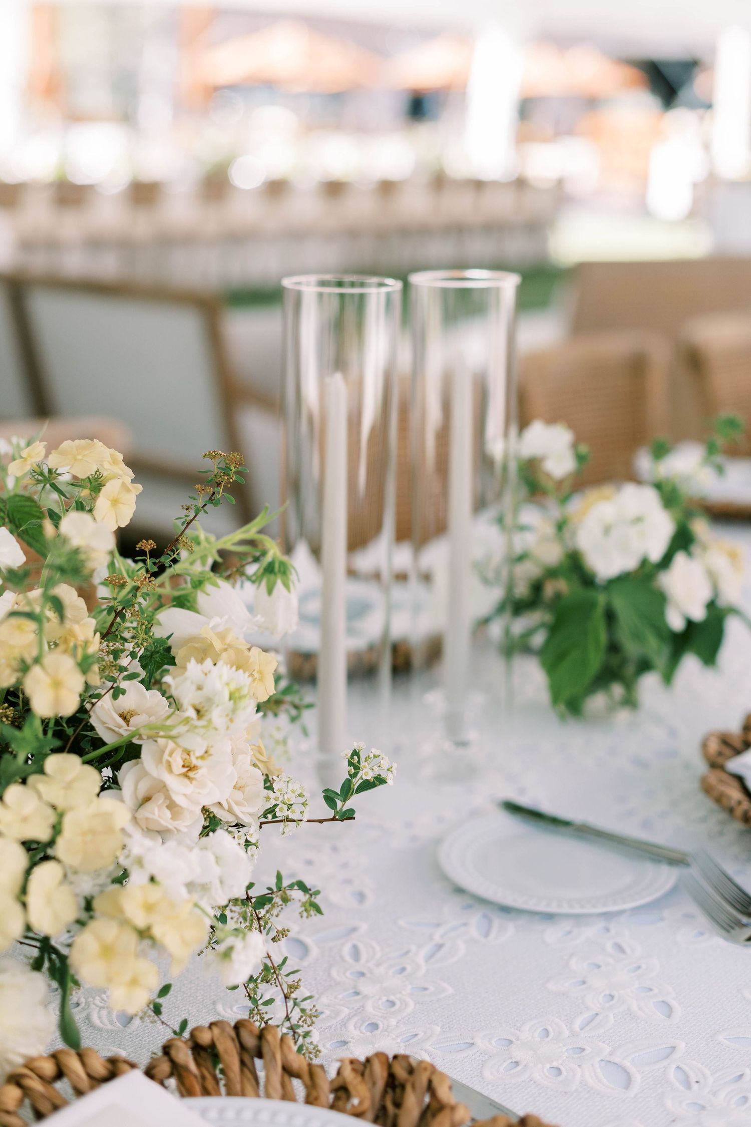 Wedding table setting with champagne flutes and white floral centerpieces on lace tablecloth.
