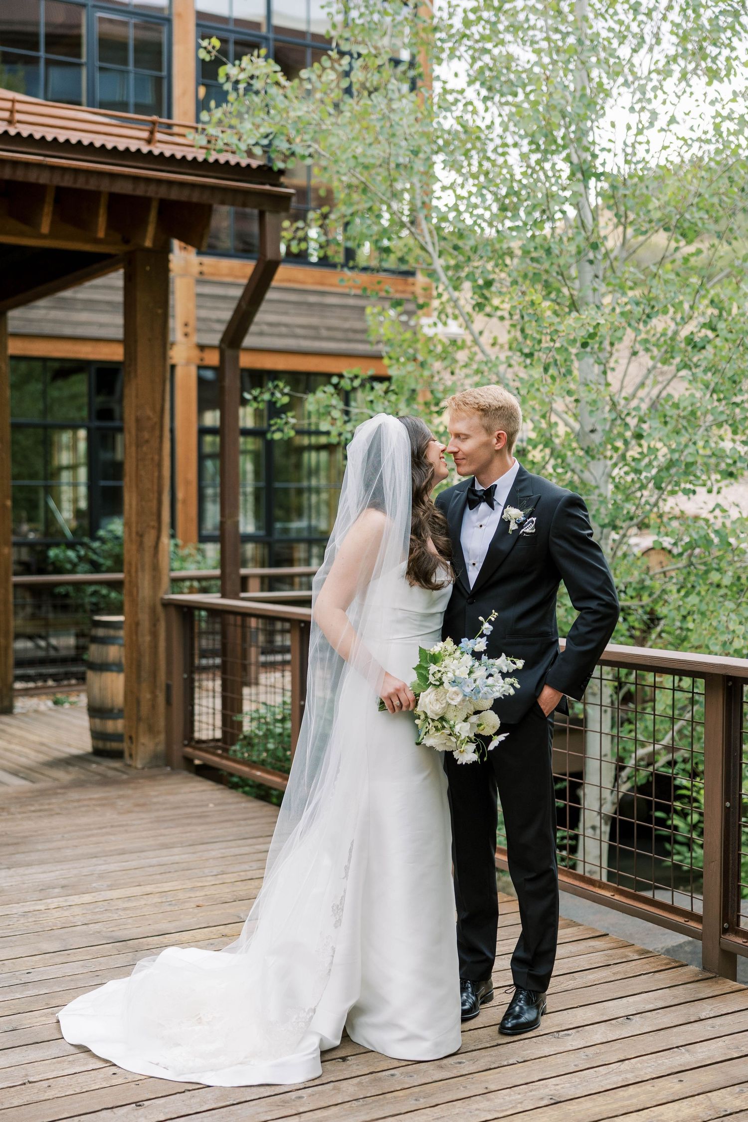 A romantic first look moment between newlyweds on a rustic wooden deck surrounded by trees.