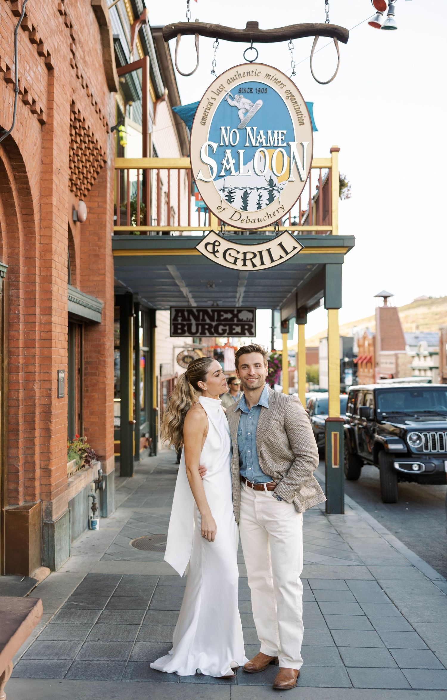 A couple poses outside a rustic brick building with restaurant signage.