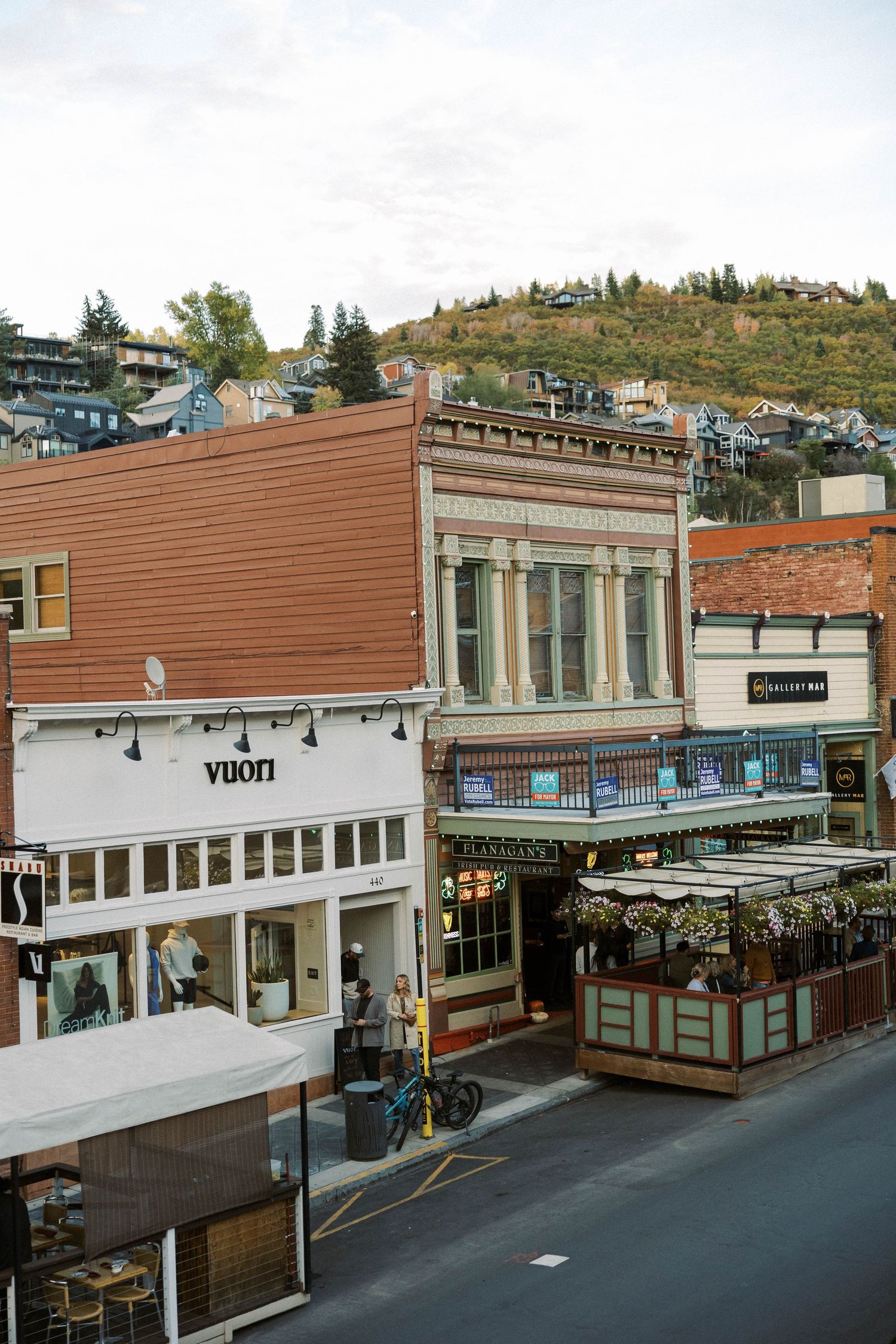 A series of connected brown and white commercial storefronts along a street in a small town business district.