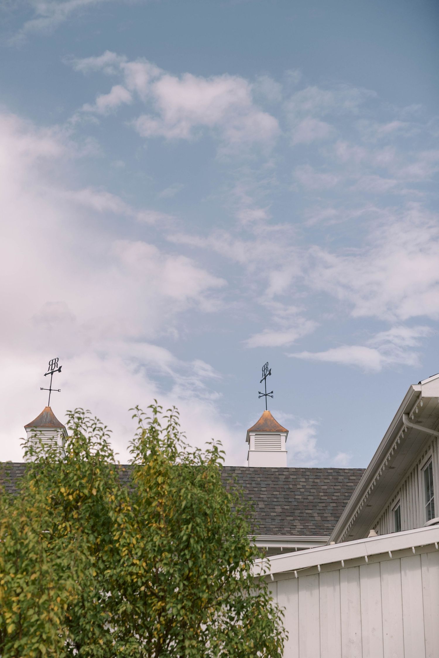 White barn-style building with cupolas on the roof against a blue sky with wispy clouds.