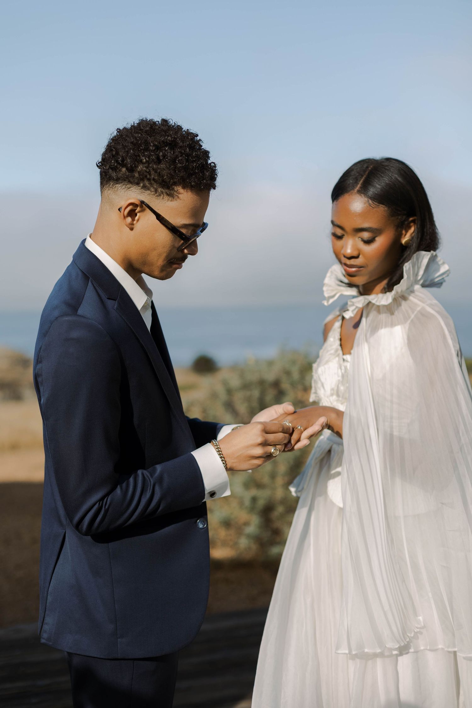 A romantic wedding ceremony moment as a couple exchanges rings against a scenic outdoor backdrop.