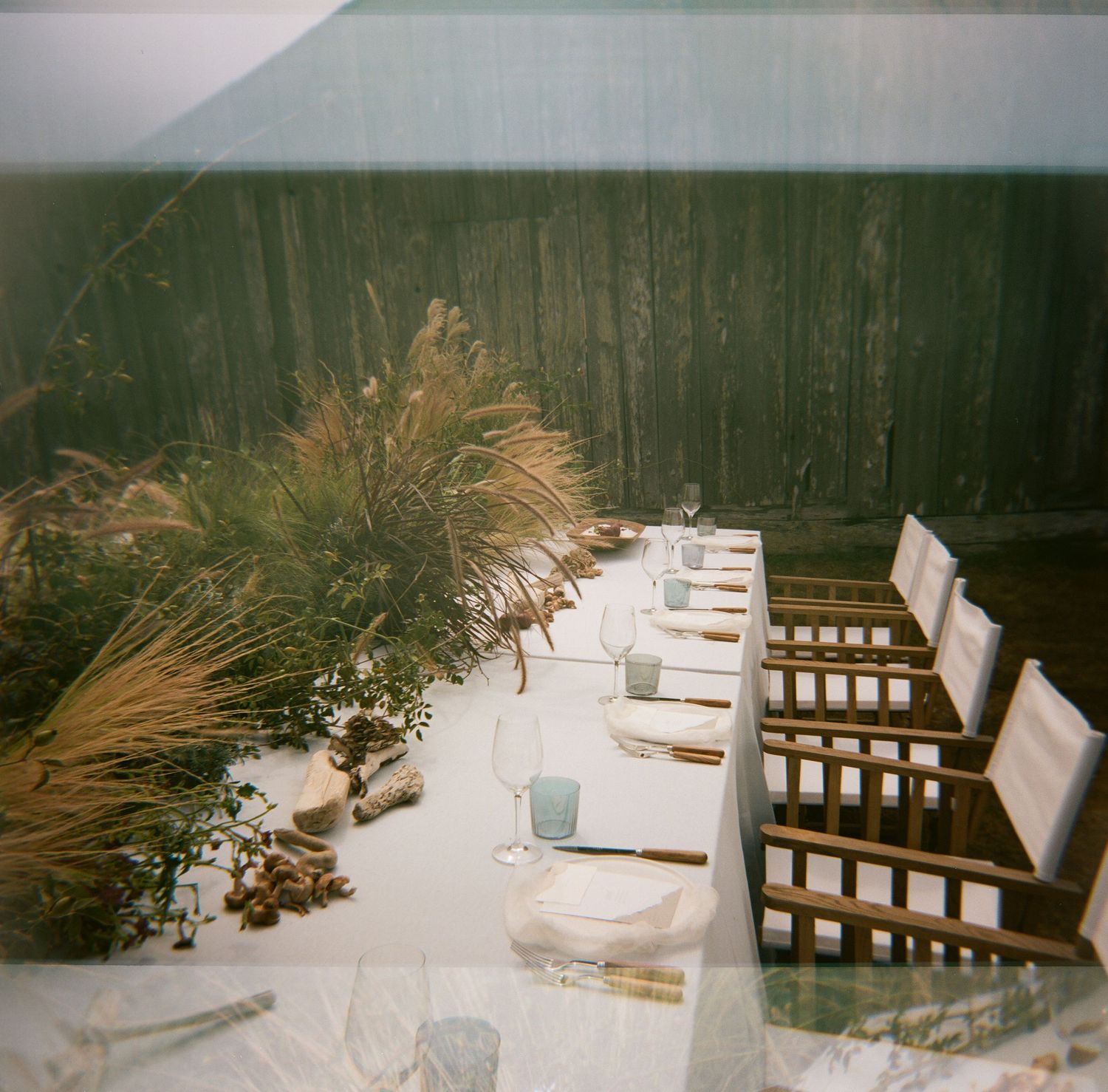 Snow covered patio furniture and deck with winter trees in the background viewed through a vintage film camera effect.