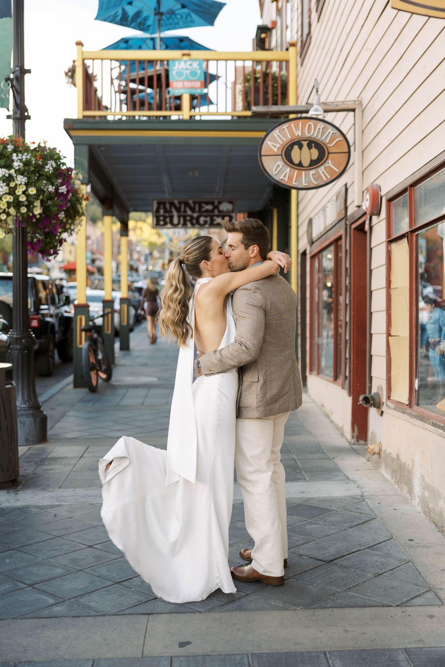 A romantic couple shares a kiss under a bright turquoise umbrella on a charming city street.