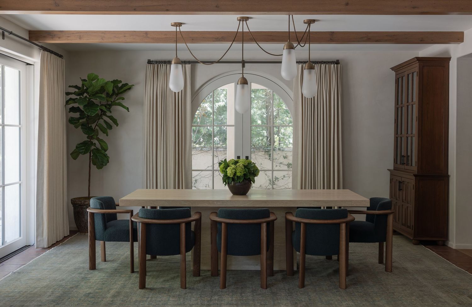 Elegant dining room with wood table, navy chairs, arched window, pendant lights, and green rug.