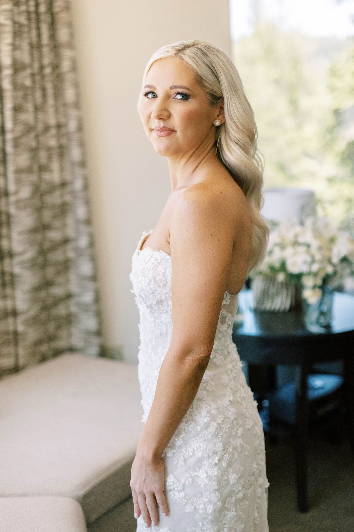A bride poses in an elegant strapless lace wedding gown with delicate beading and embellishments.