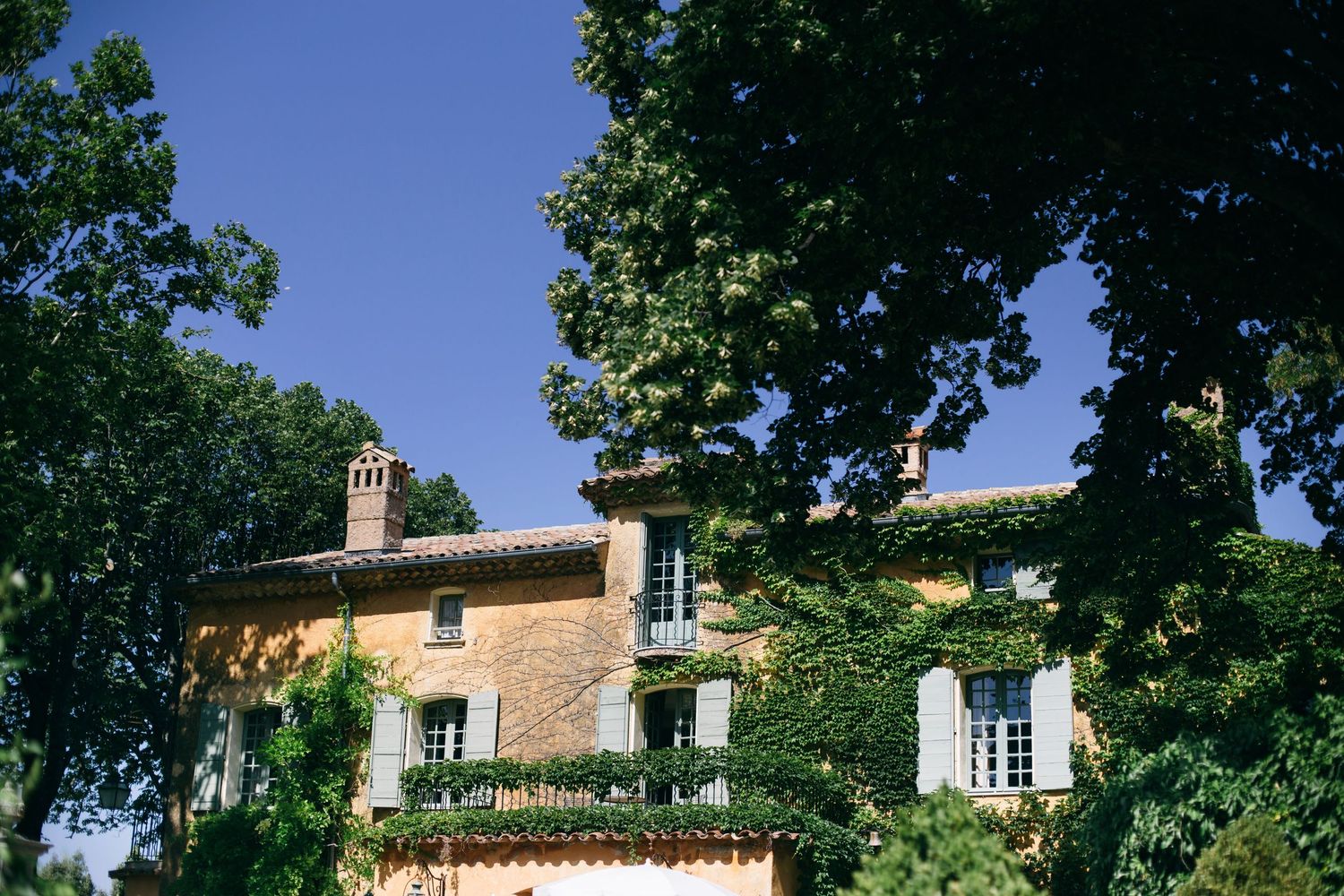 Traditional Mediterranean villa with ivy-covered walls and blue shutters against a bright summer sky.