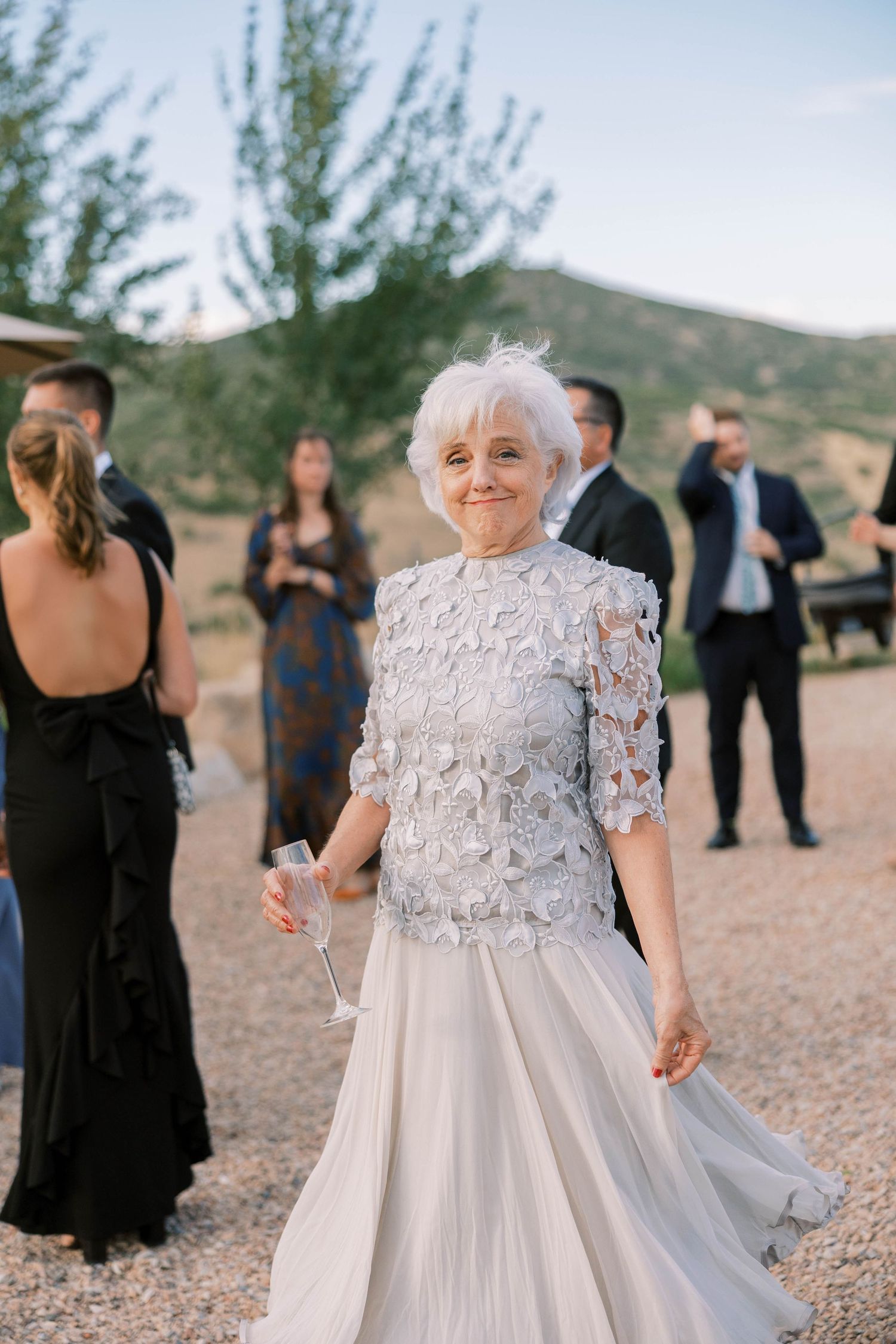 Wedding guests in formal attire gather outdoors on desert terrain with mountains in background.