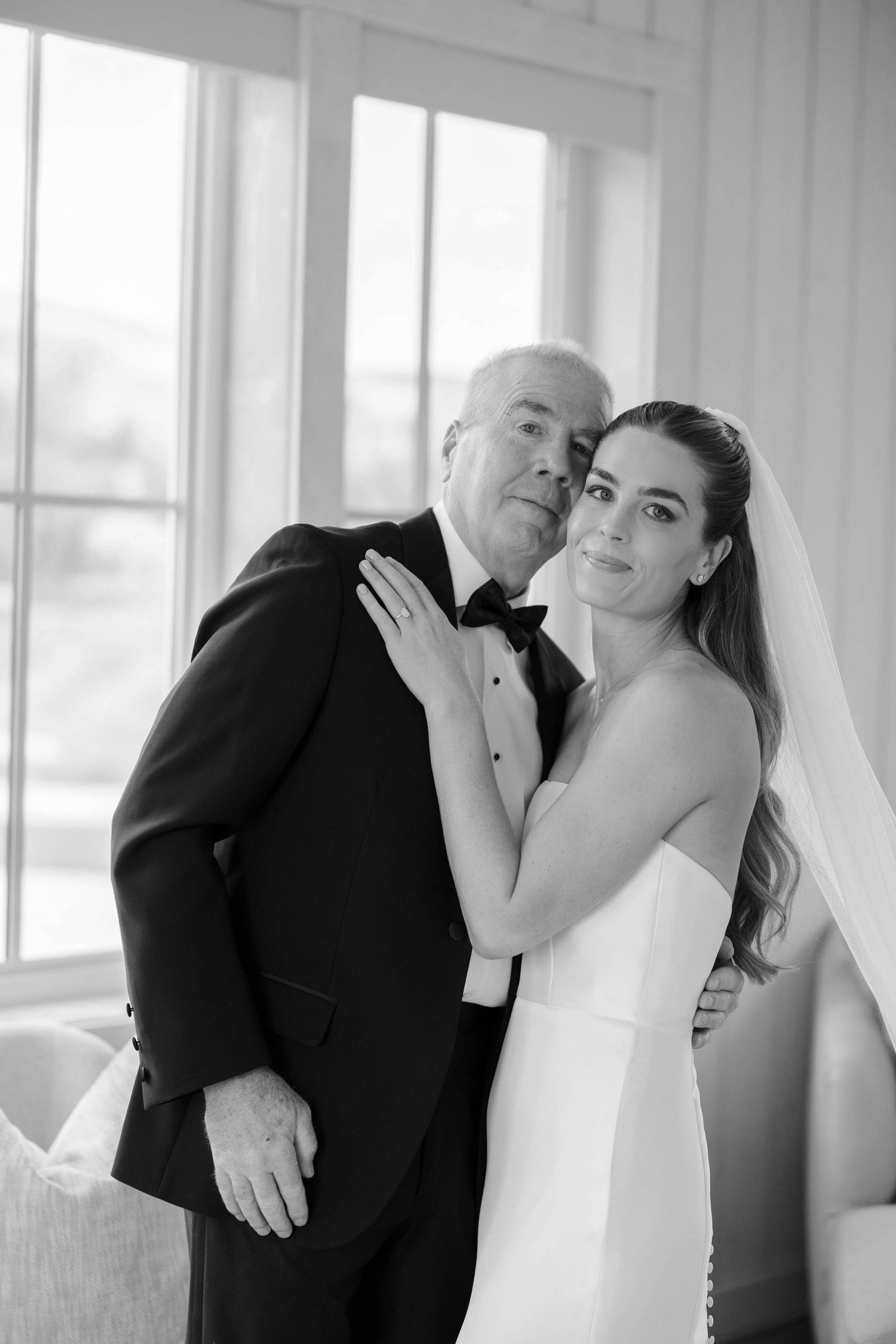 Wedding party in formal attire posing by bright windows in an elegant white room.