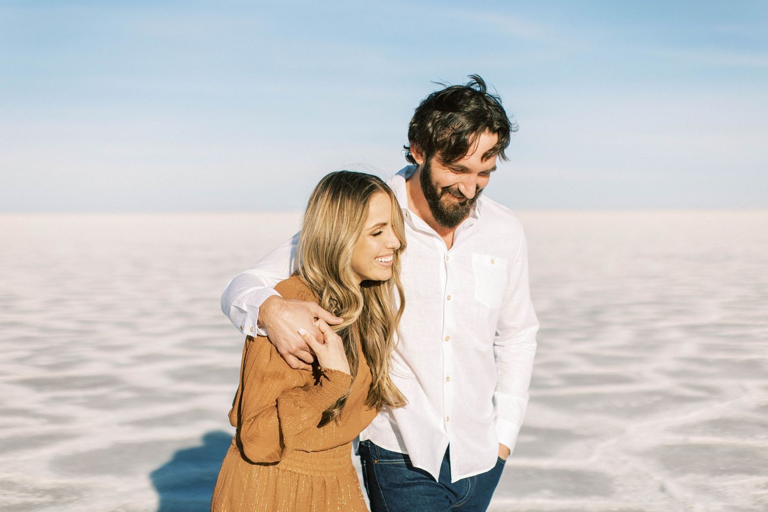 Couple in casual attire sharing an intimate moment on salt flats under blue sky.