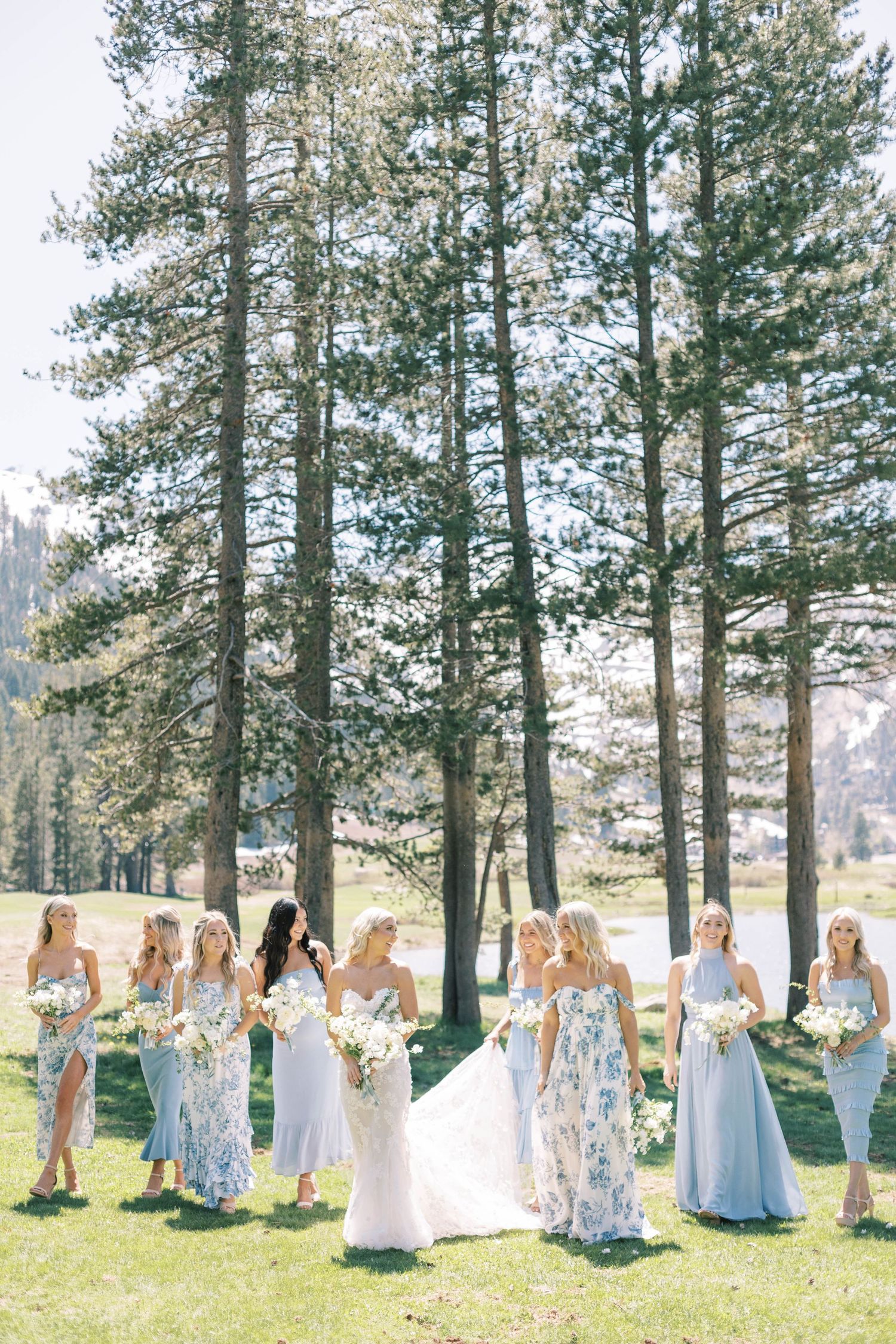 Bridesmaids in blue floral dresses pose with bouquets against a backdrop of mountain pines.