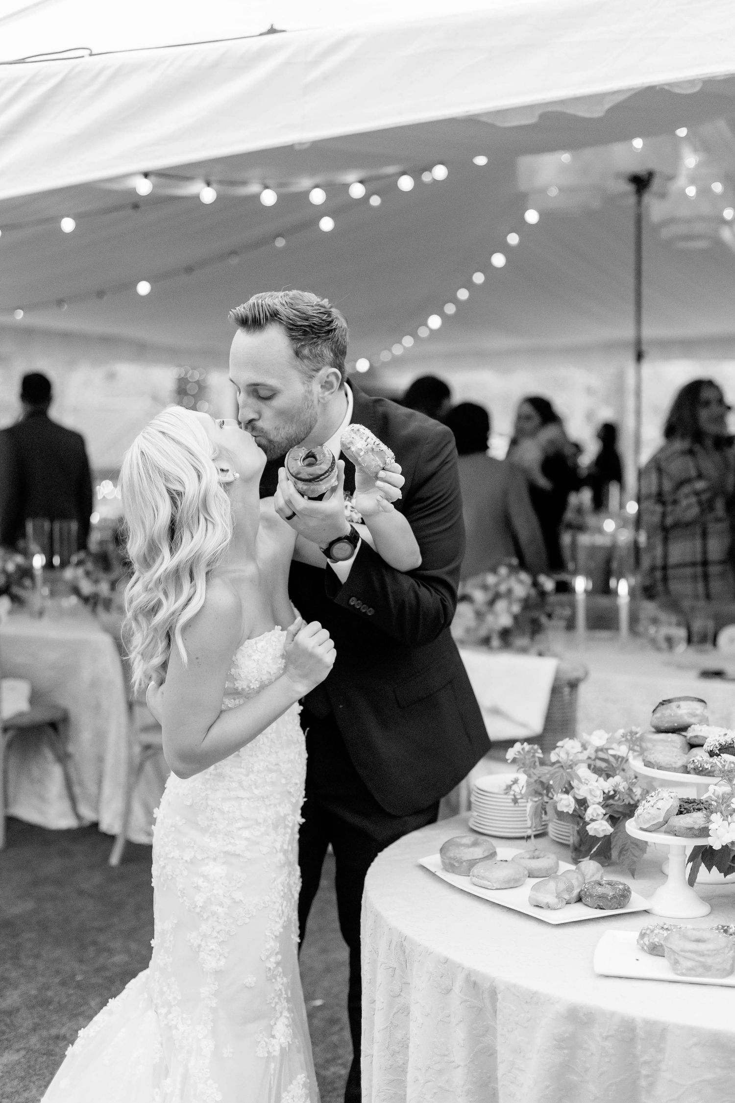 Tender moment between newlyweds sharing dessert at their wedding reception under twinkling lights.