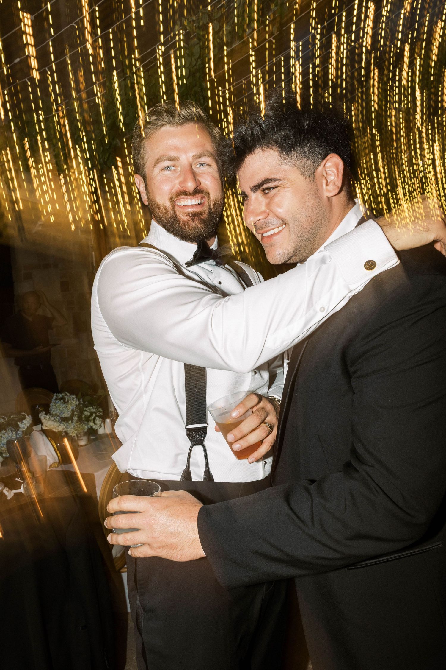 Groomsmen celebrating and embracing on a dance floor with golden string lights overhead.