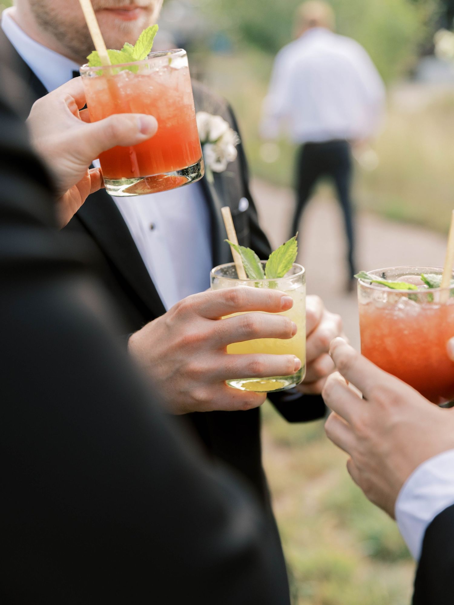 People enjoying colorful cocktails garnished with celery and citrus at an outdoor gathering.