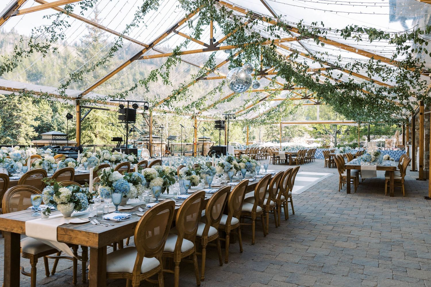 Elegant outdoor wedding reception setup with long tables under white floral canopy and string lights creating romantic ambiance.